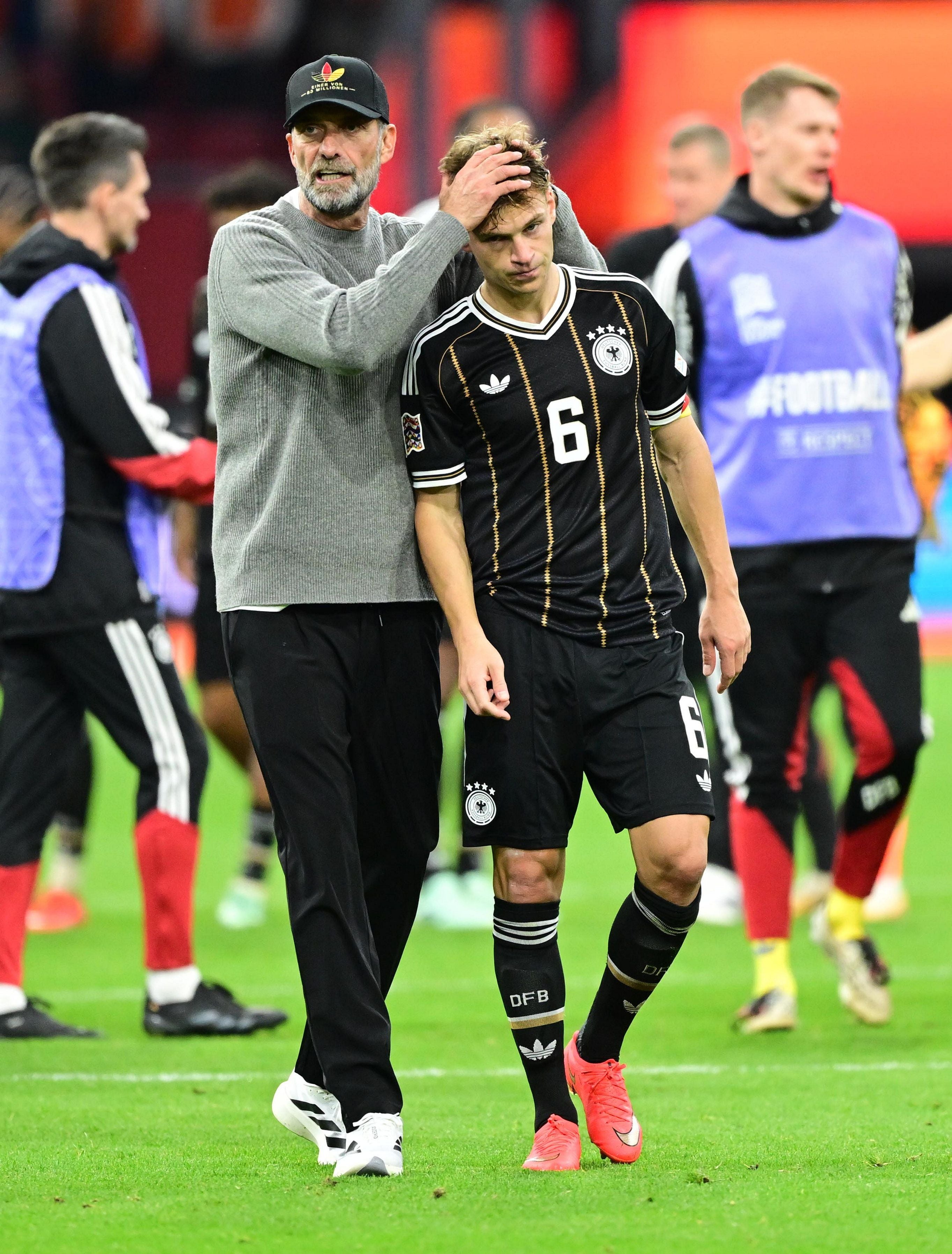 Trainer tröstet einen enttäuschten deutschen Fußballspieler auf dem Spielfeld.