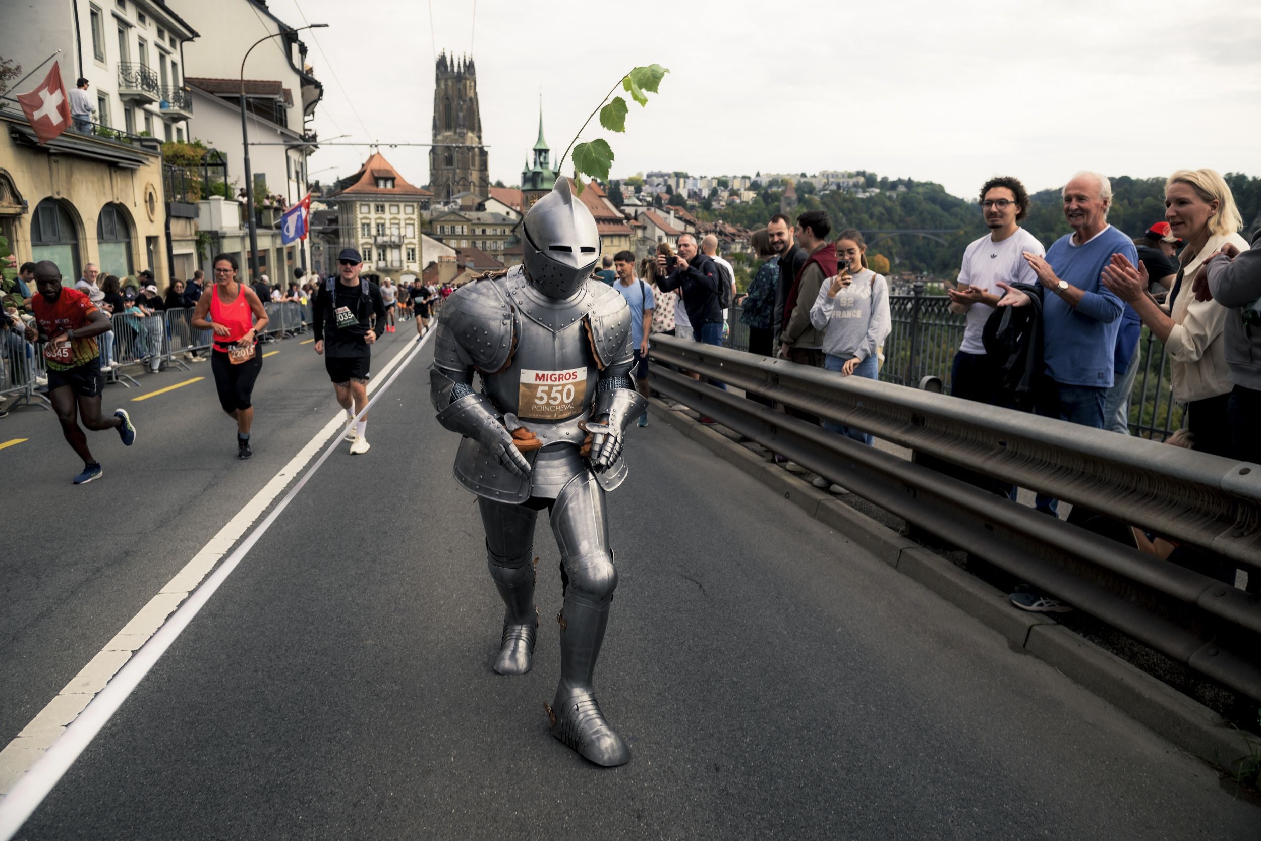 Ein Läufer in Ritterrüstung nimmt am Murtenlauf teil, Zuschauer applaudieren am Straßenrand.