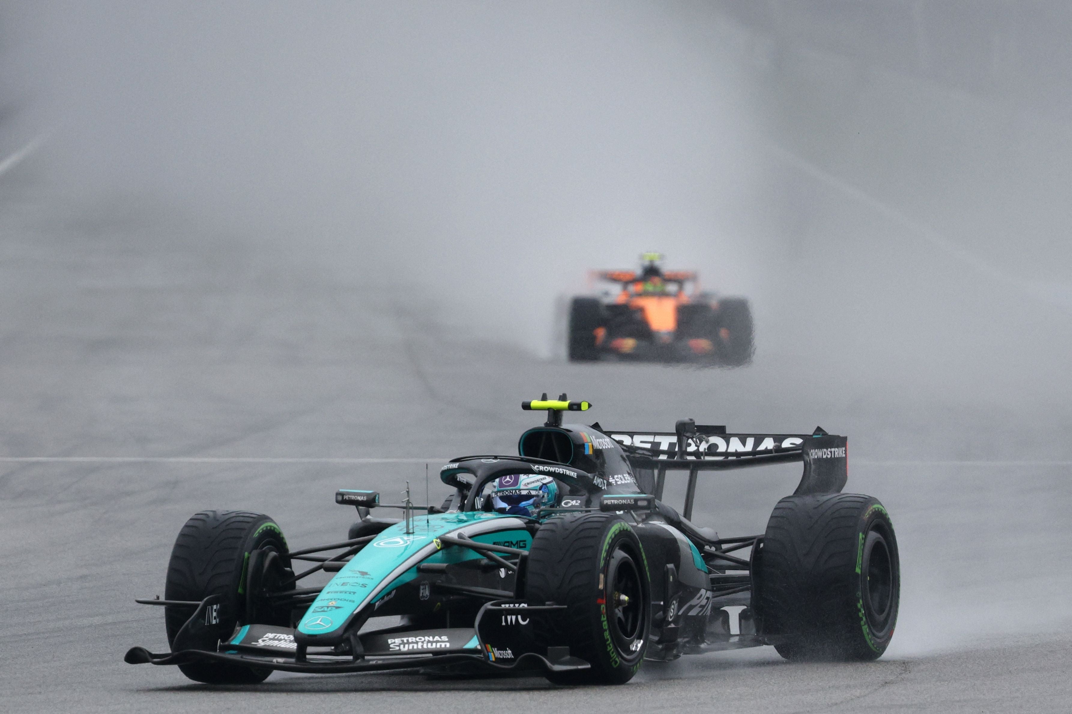 Ein Mercedes-Formel-1-Auto fährt bei Regen auf nasser Strecke, ein anderes Auto folgt im Hintergrund.