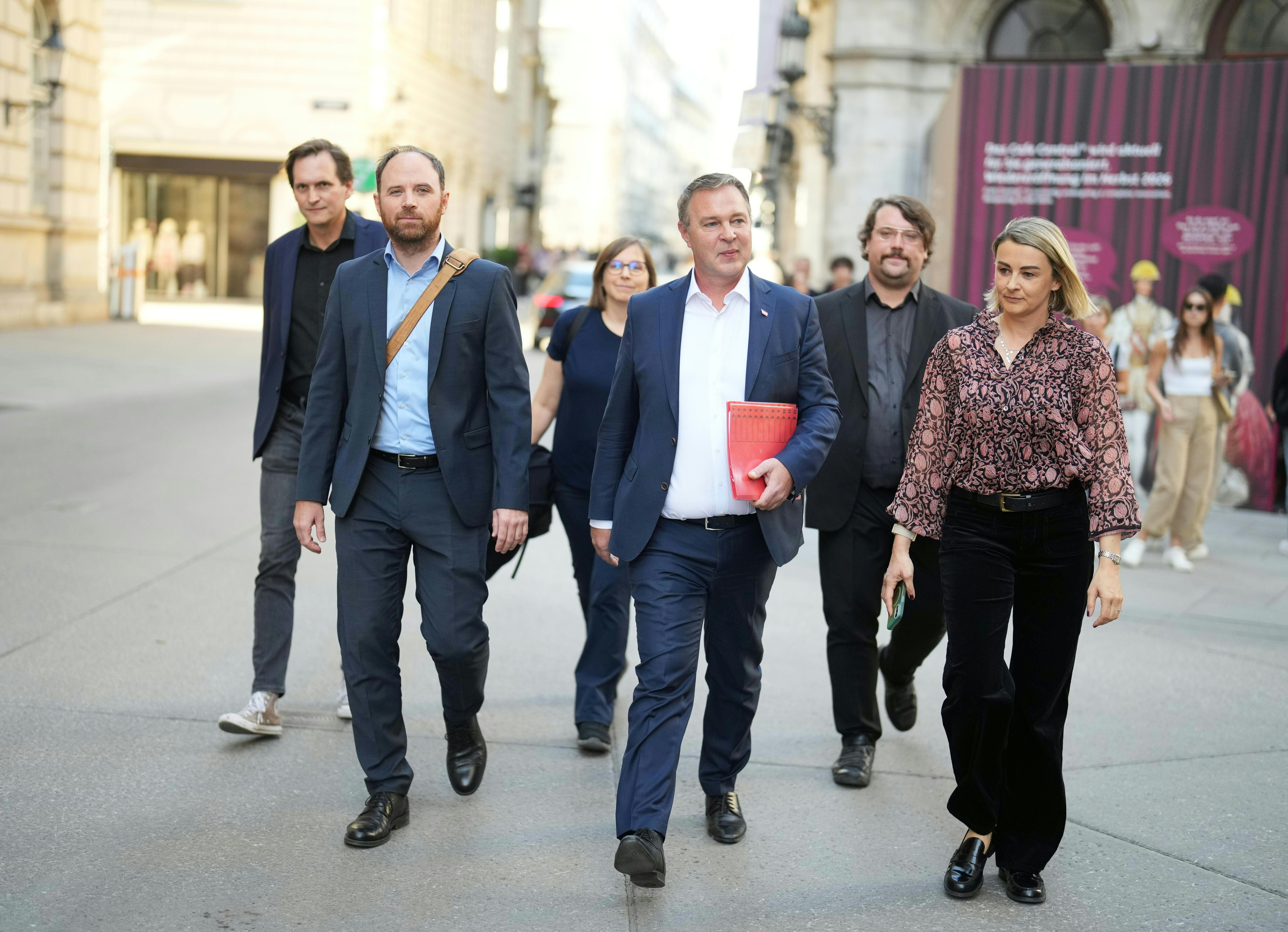 Sechs Erwachsene gehen in Businesskleidung gemeinsam eine Straße entlang.