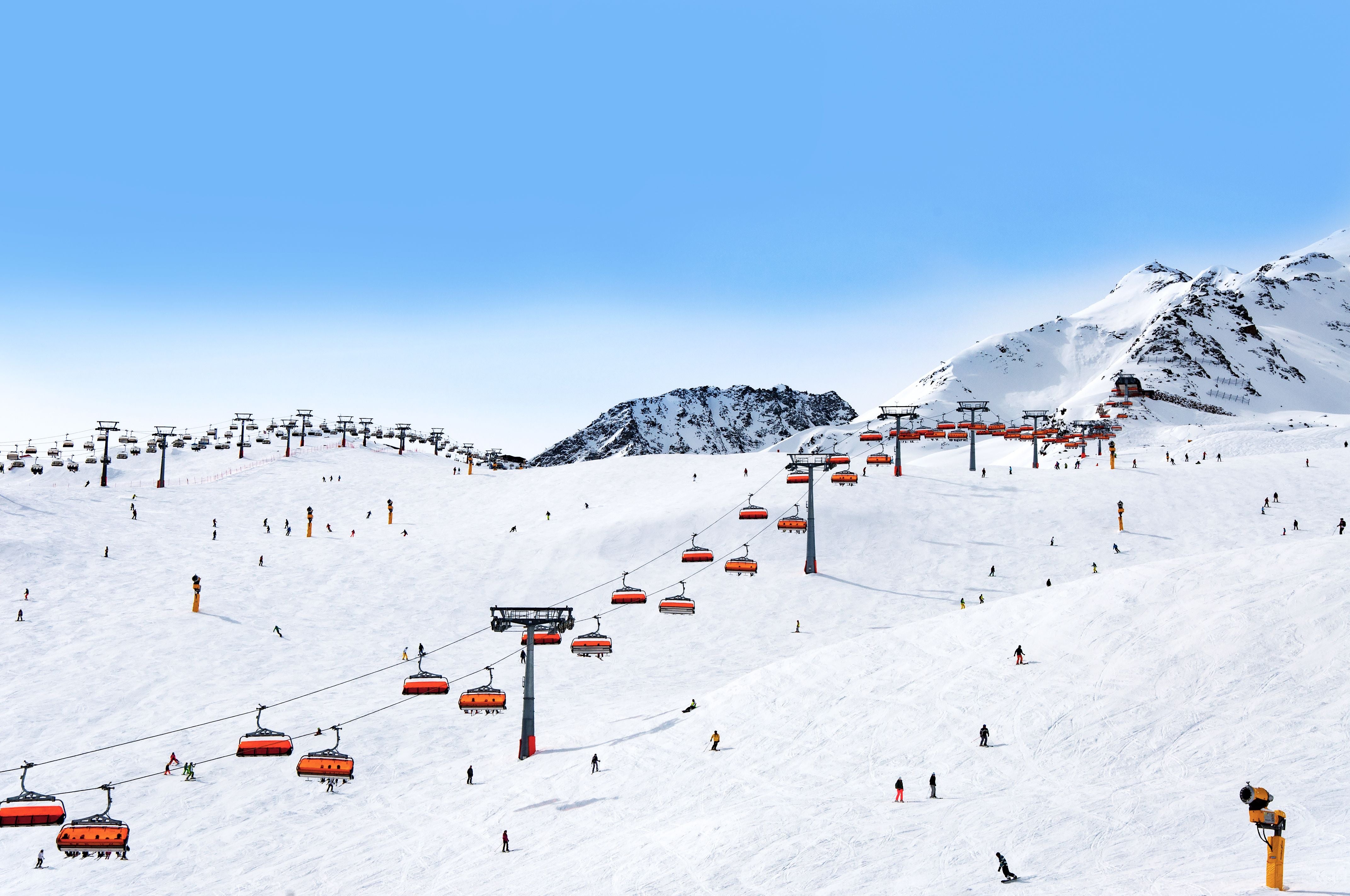 Viele Skifahrer und orangefarbene Sessellifte in einem verschneiten Skigebiet der Alpen.