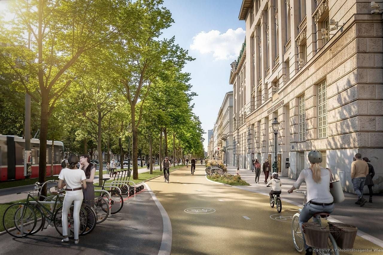 Menschen fahren Fahrrad und spazieren auf einer begrünten, neu gestalteten Wiener Ringstraße.