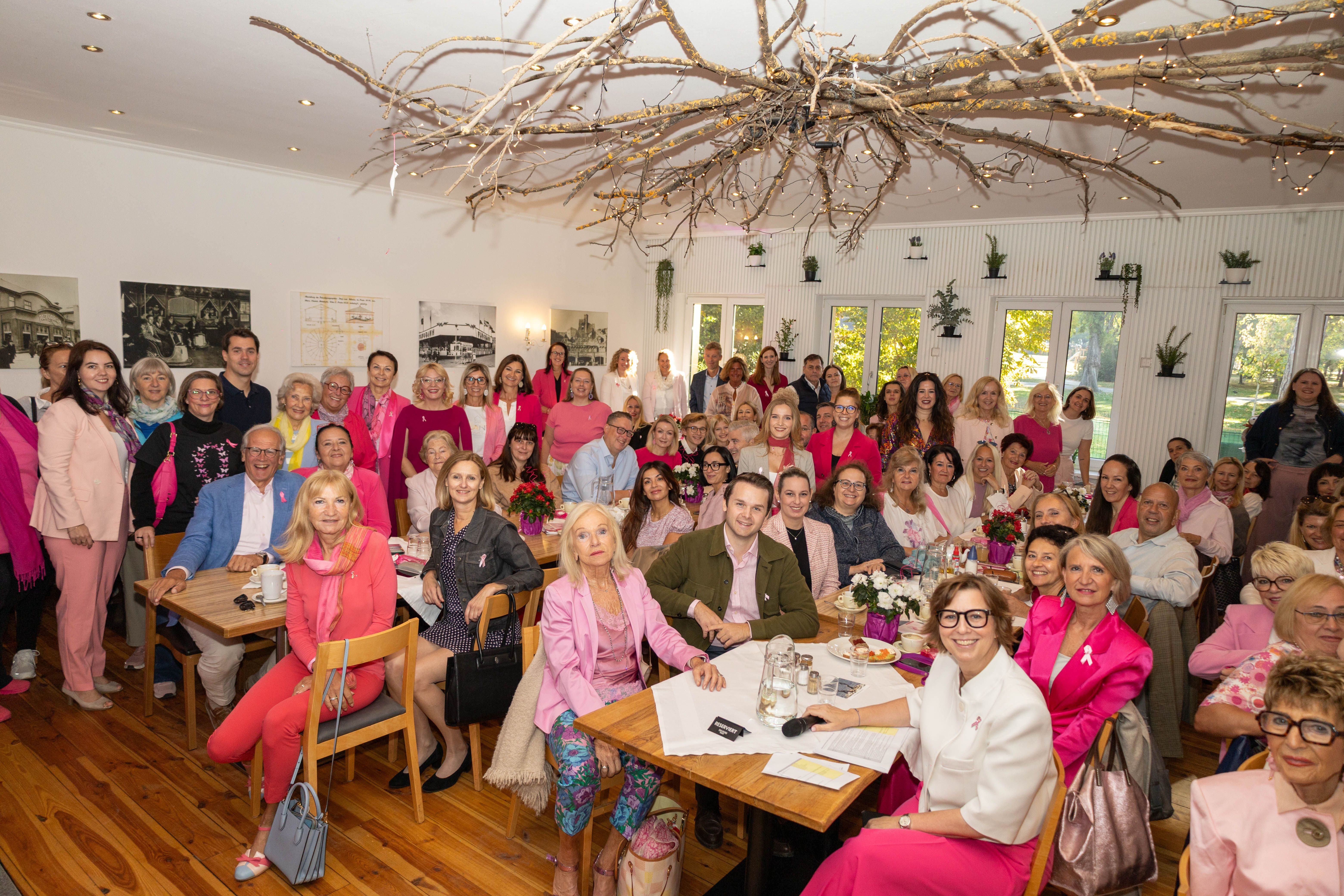 Große Gruppe von Menschen beim Pink Ribbon Breakfast Club, viele tragen rosa Kleidung.