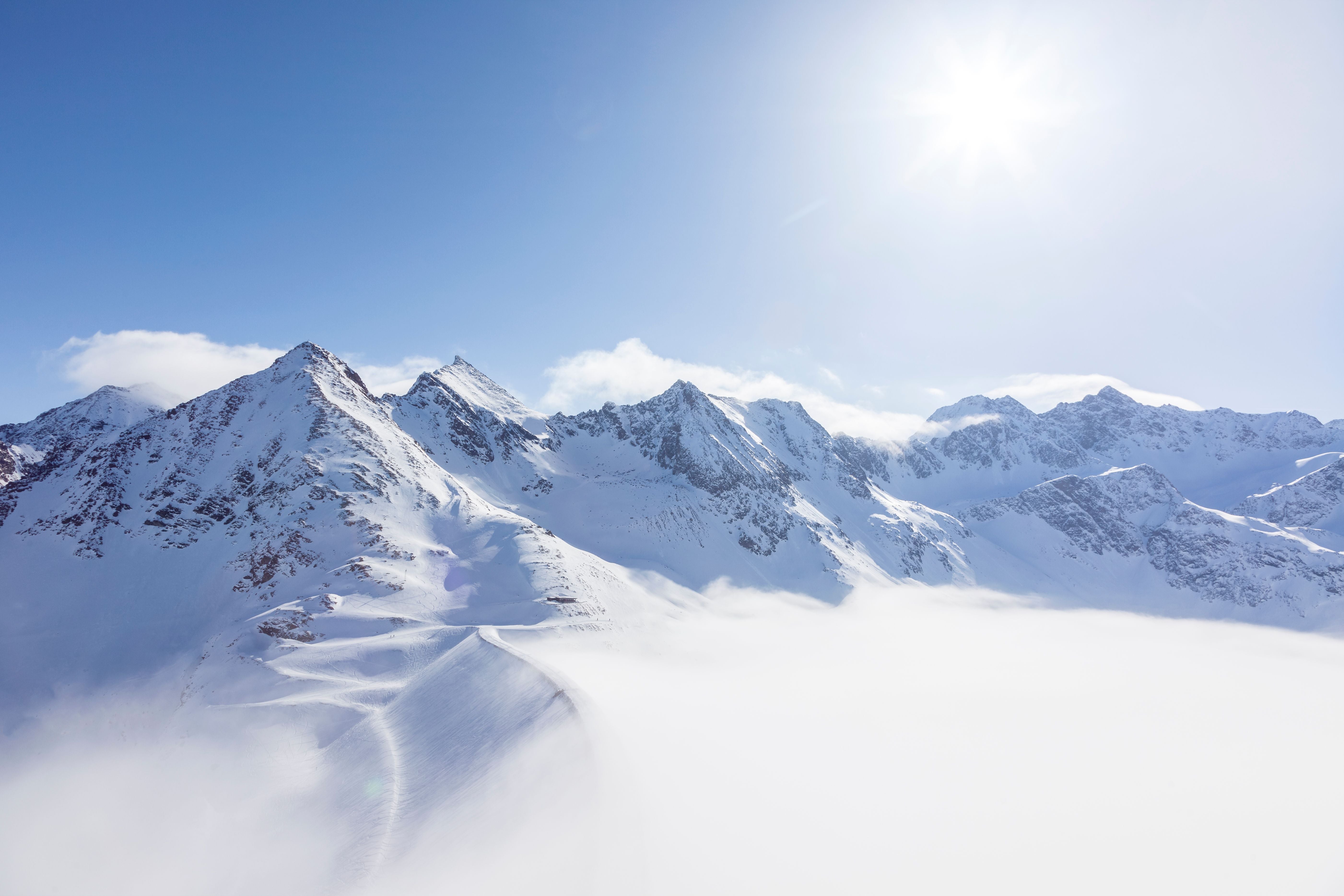 Sonnige schneebedeckte Berge mit Wolken im Tal darunter.