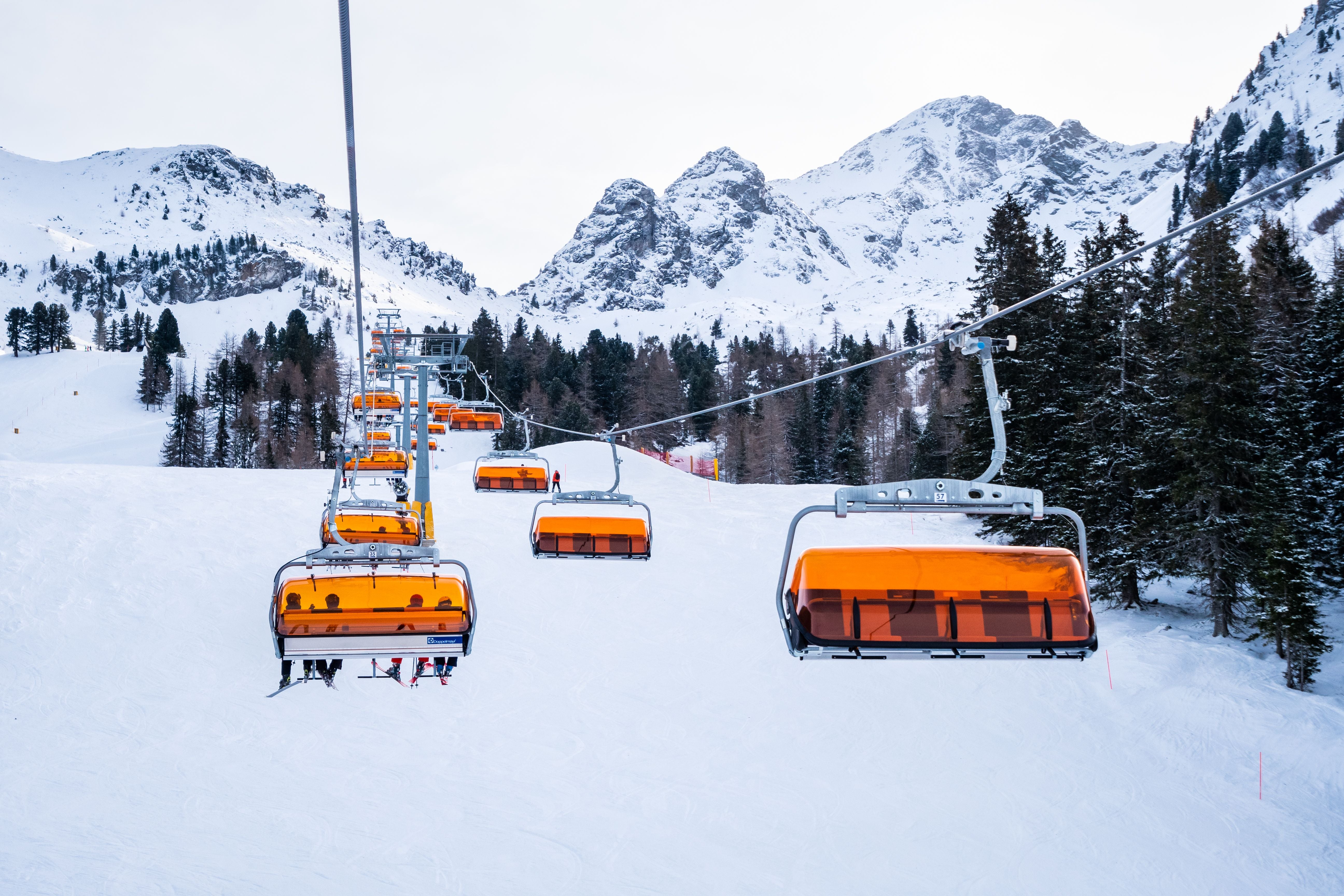 Sessellift mit orangefarbenen Schutzhauben fährt durch verschneite Berglandschaft in Österreich.