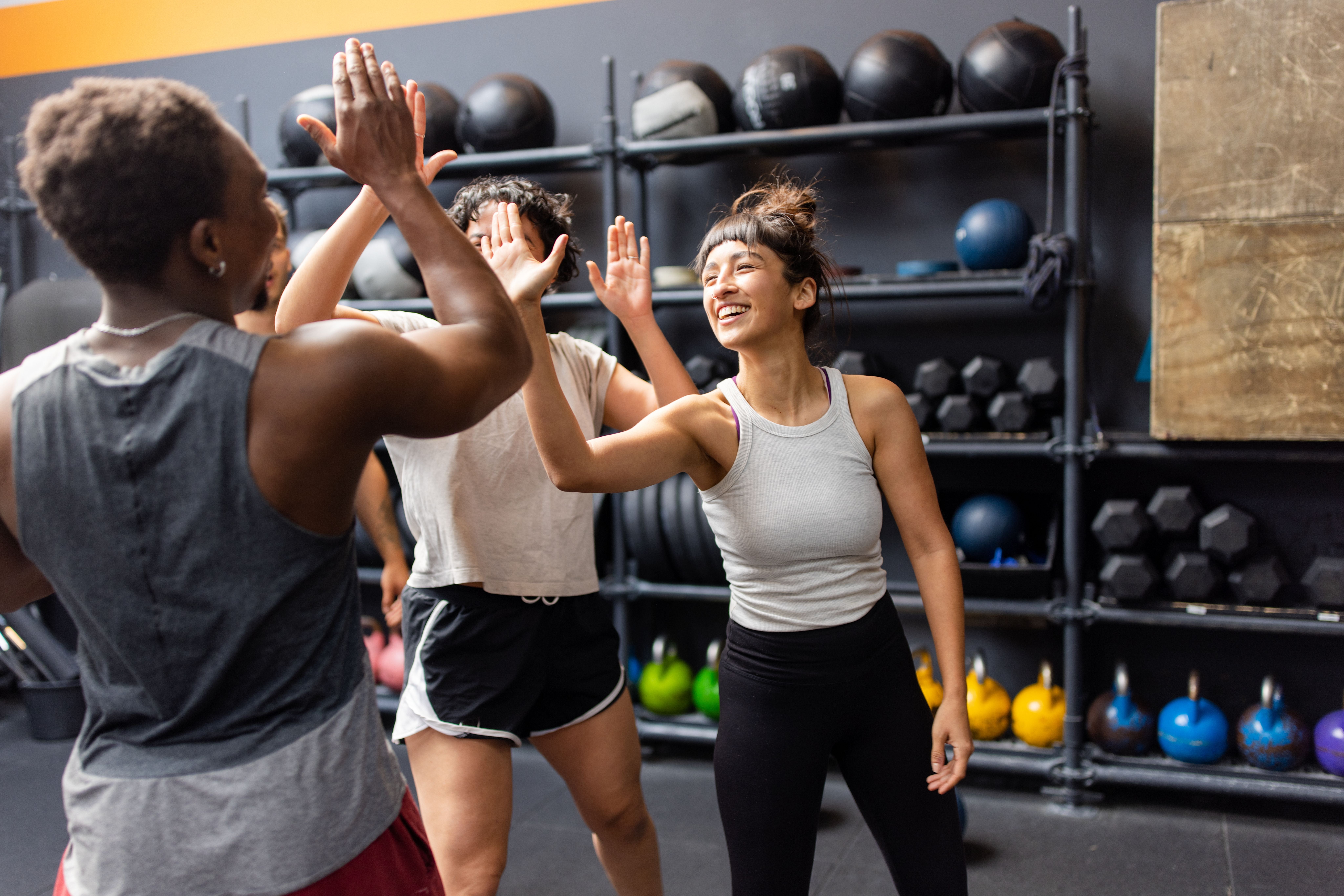 Drei junge Menschen geben sich im Fitnessstudio nach dem Training lachend High-Fives.