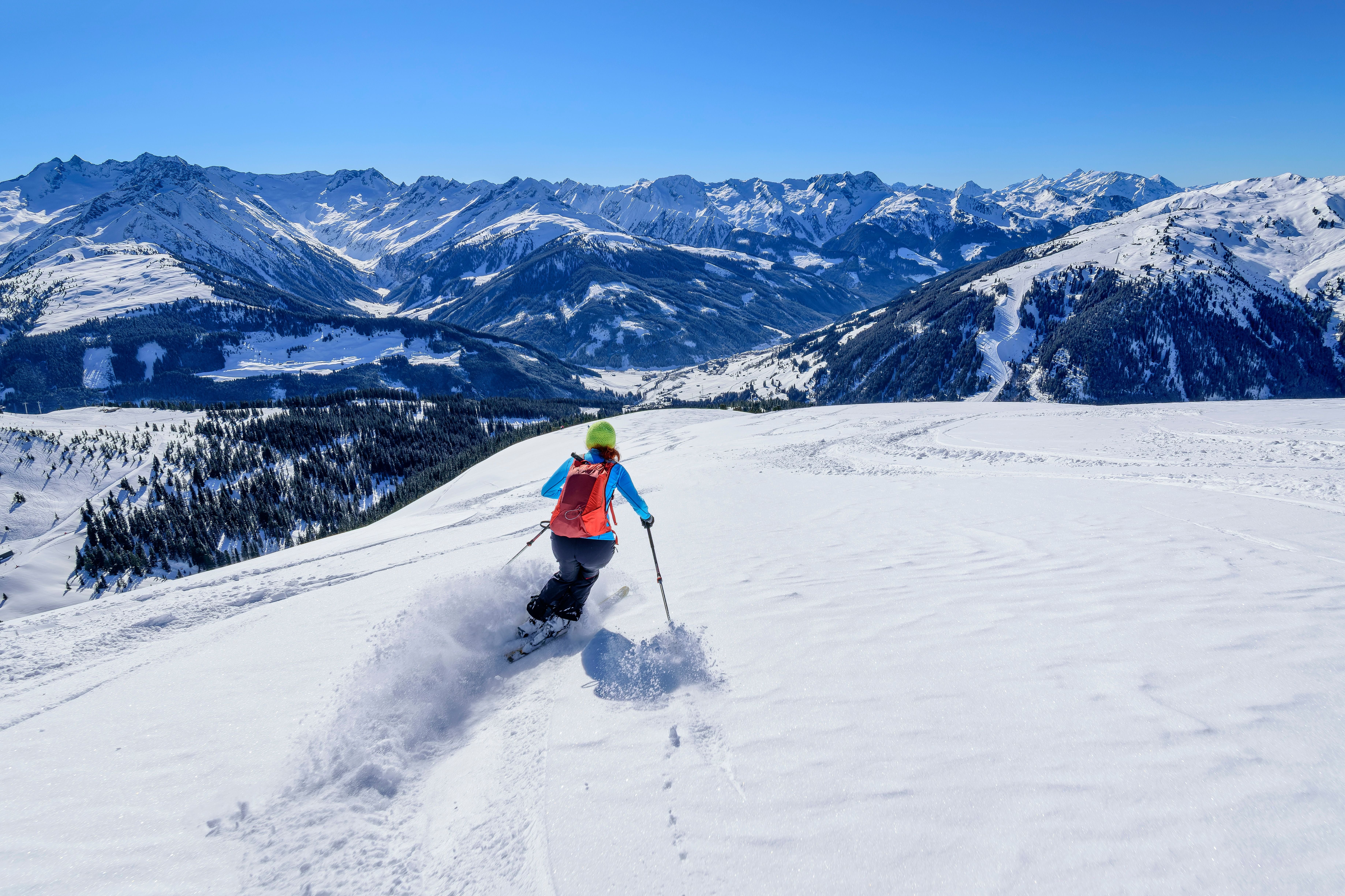 Skifahrer fährt durch frischen Pulverschnee mit Tiroler Alpen im Hintergrund.