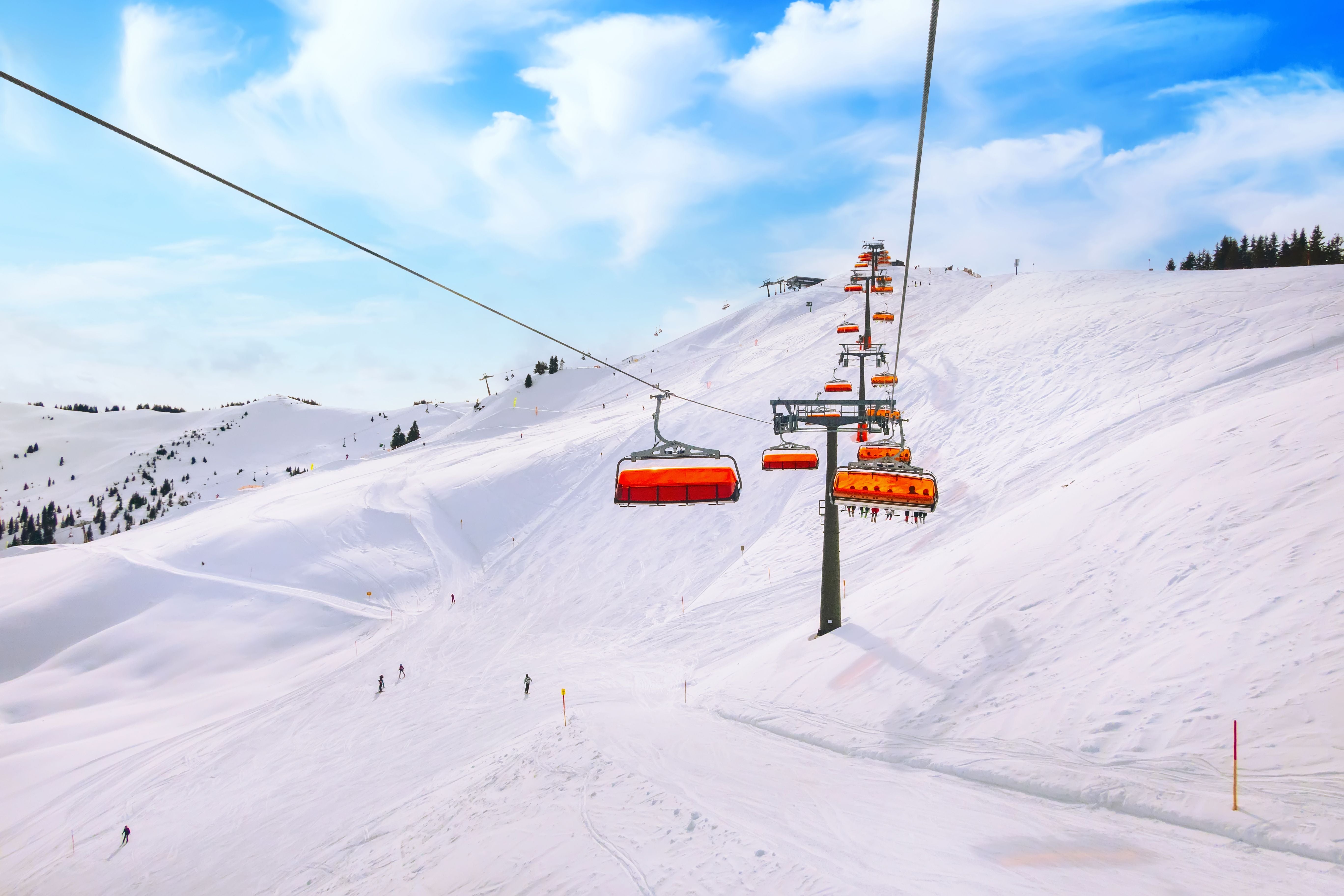 Skilift mit orangefarbenen Sesseln über einer verschneiten Piste im Skigebiet Saalbach, Österreich.
