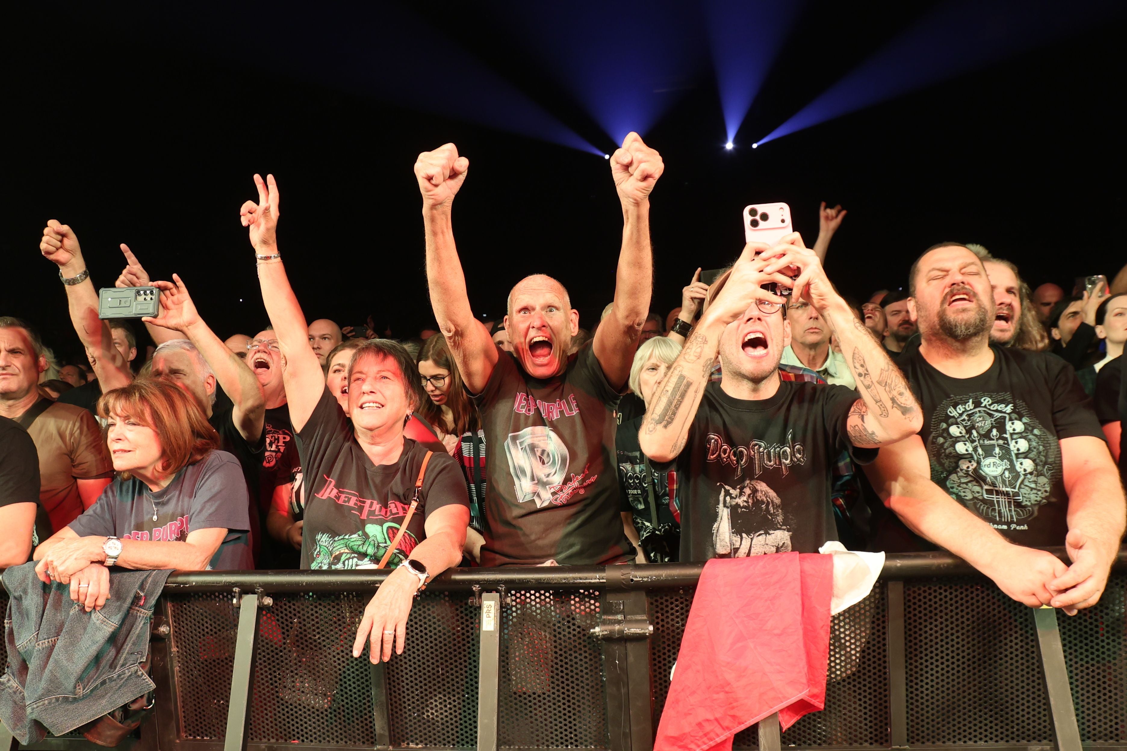 Begeisterte Deep Purple-Fans jubeln und fotografieren in der ersten Reihe bei einem Konzert.