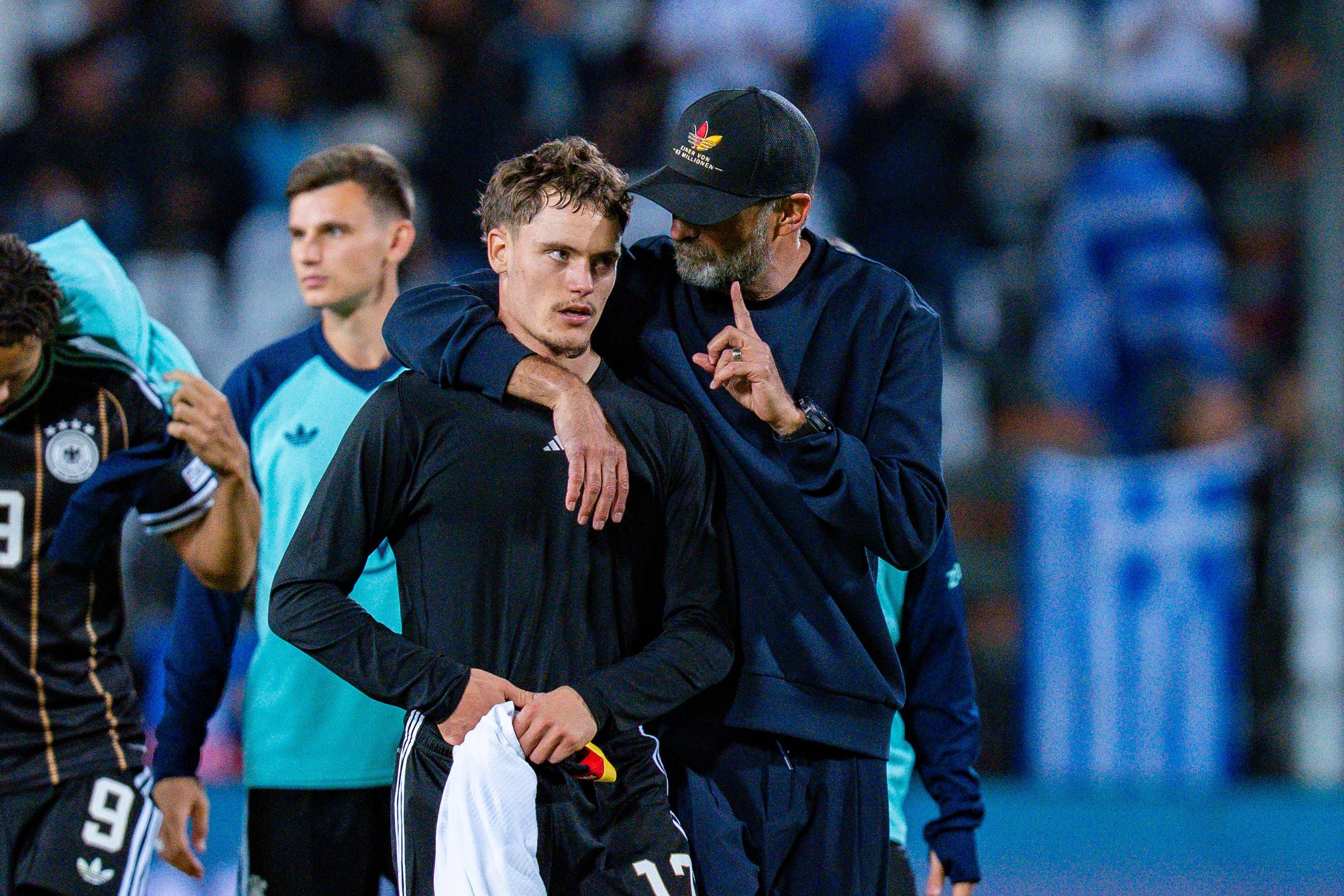 Ein Fußballtrainer spricht aufmunternd mit einem deutschen Spieler nach dem Spiel im Stadion.
