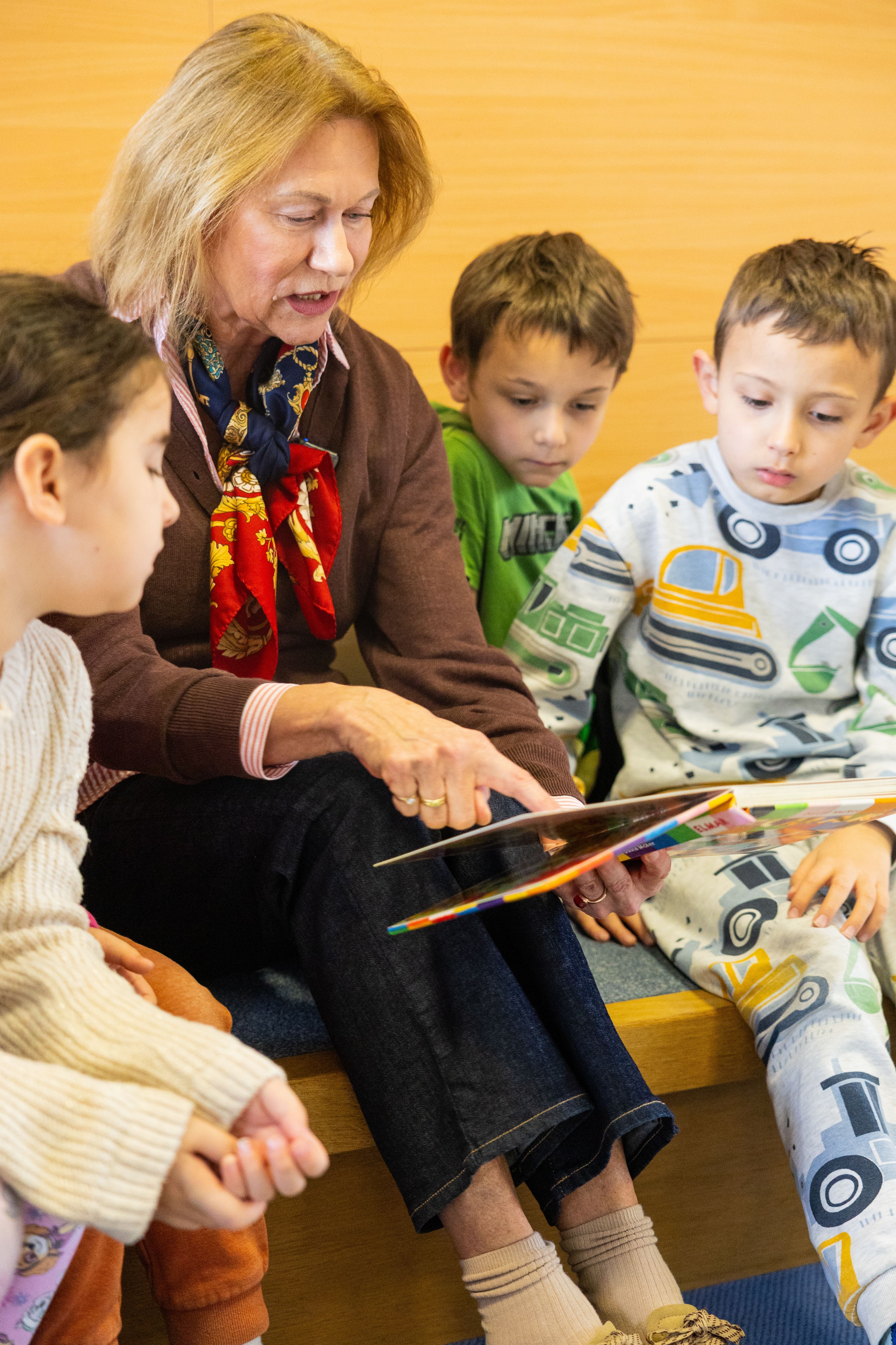 Eine Frau liest drei Kindern aus einem Buch vor, alle schauen aufmerksam zu.