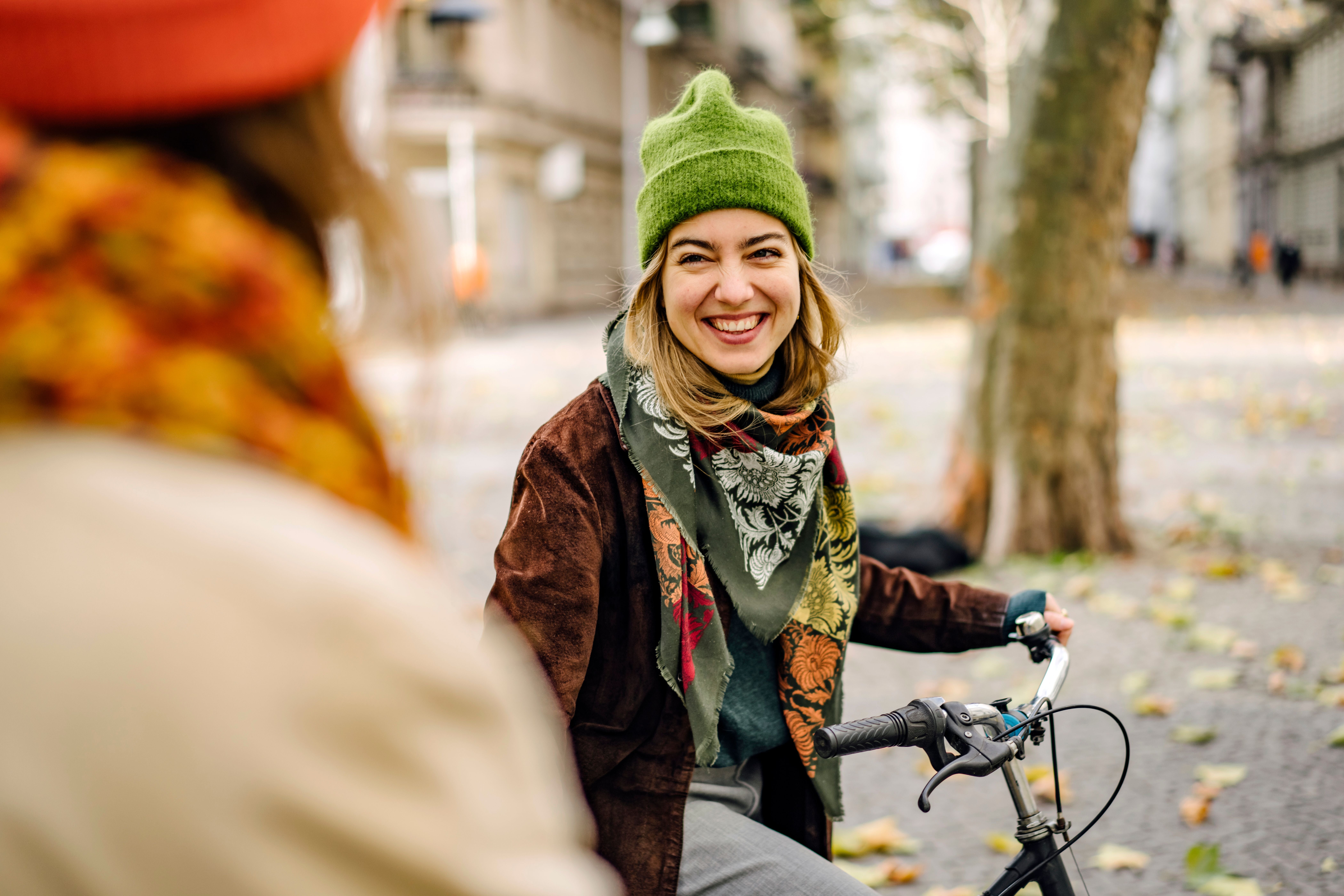 Junge Frau mit grüner Mütze lächelt auf einem Fahrrad im herbstlichen Stadtpark.