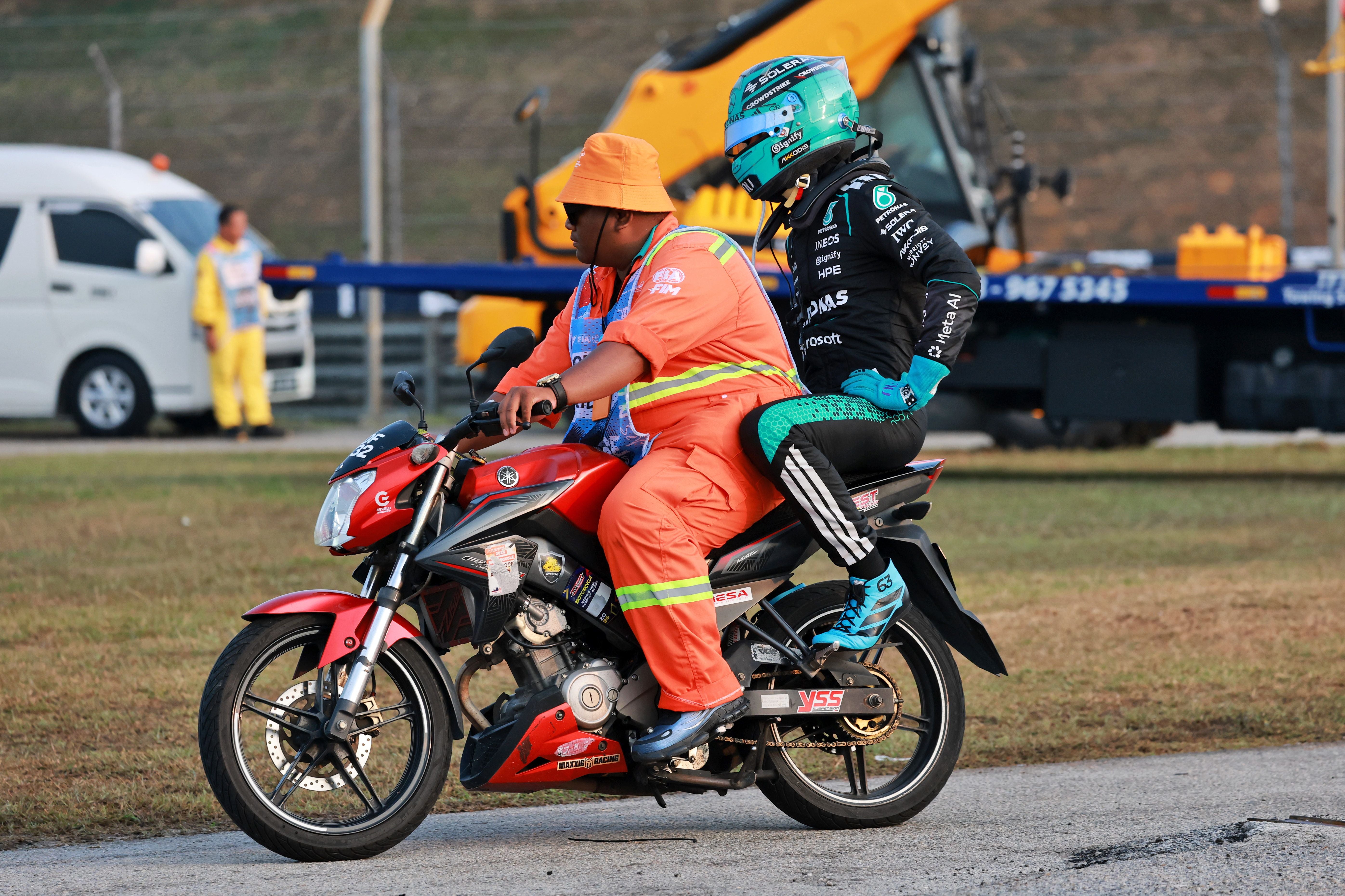 Ein Formel-1-Fahrer fährt mit einem Streckenposten auf einem roten Motorrad über die Rennstrecke.