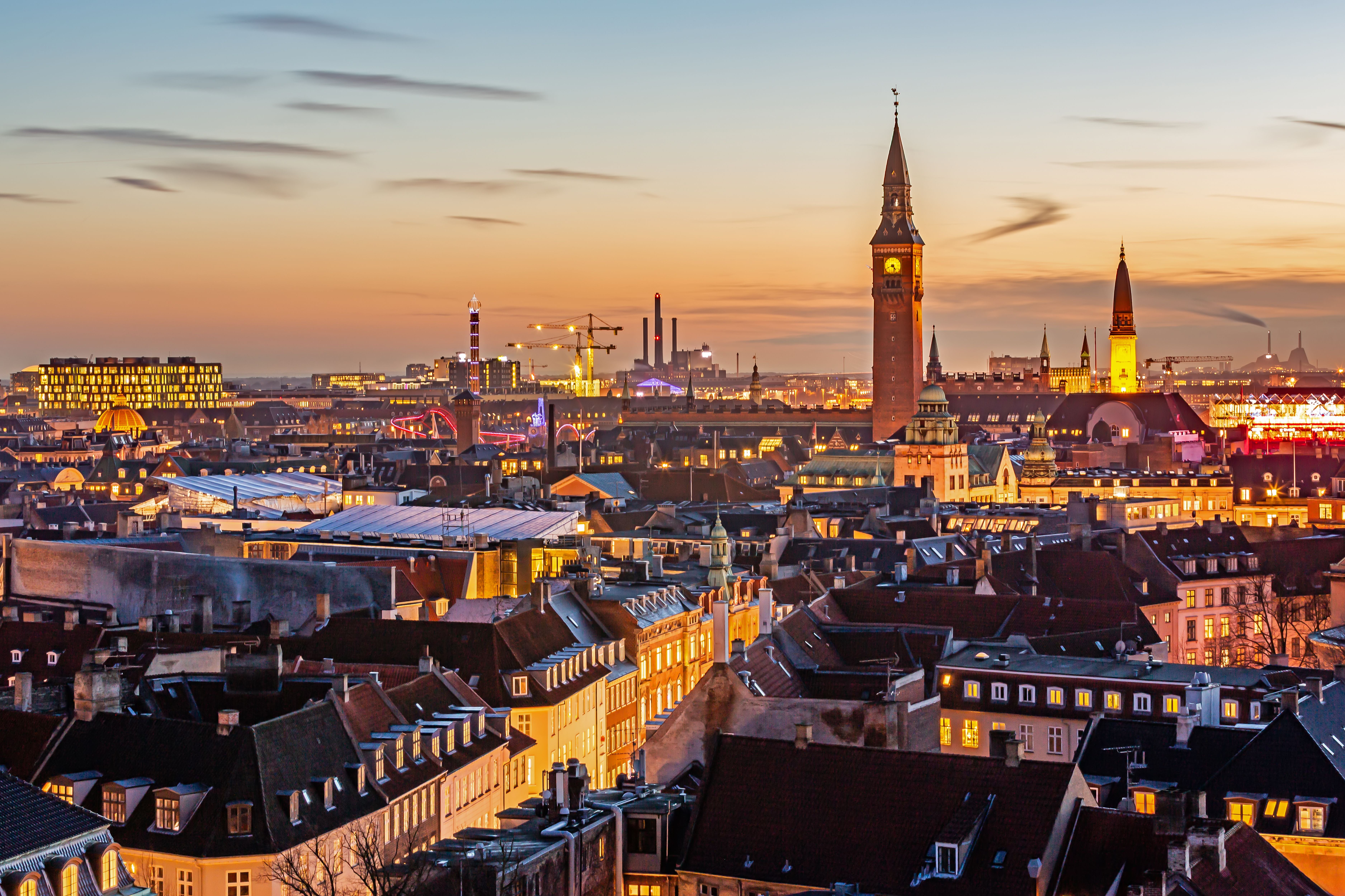 Kopenhagener Skyline bei Sonnenuntergang mit beleuchteten Gebäuden und markanten Türmen.