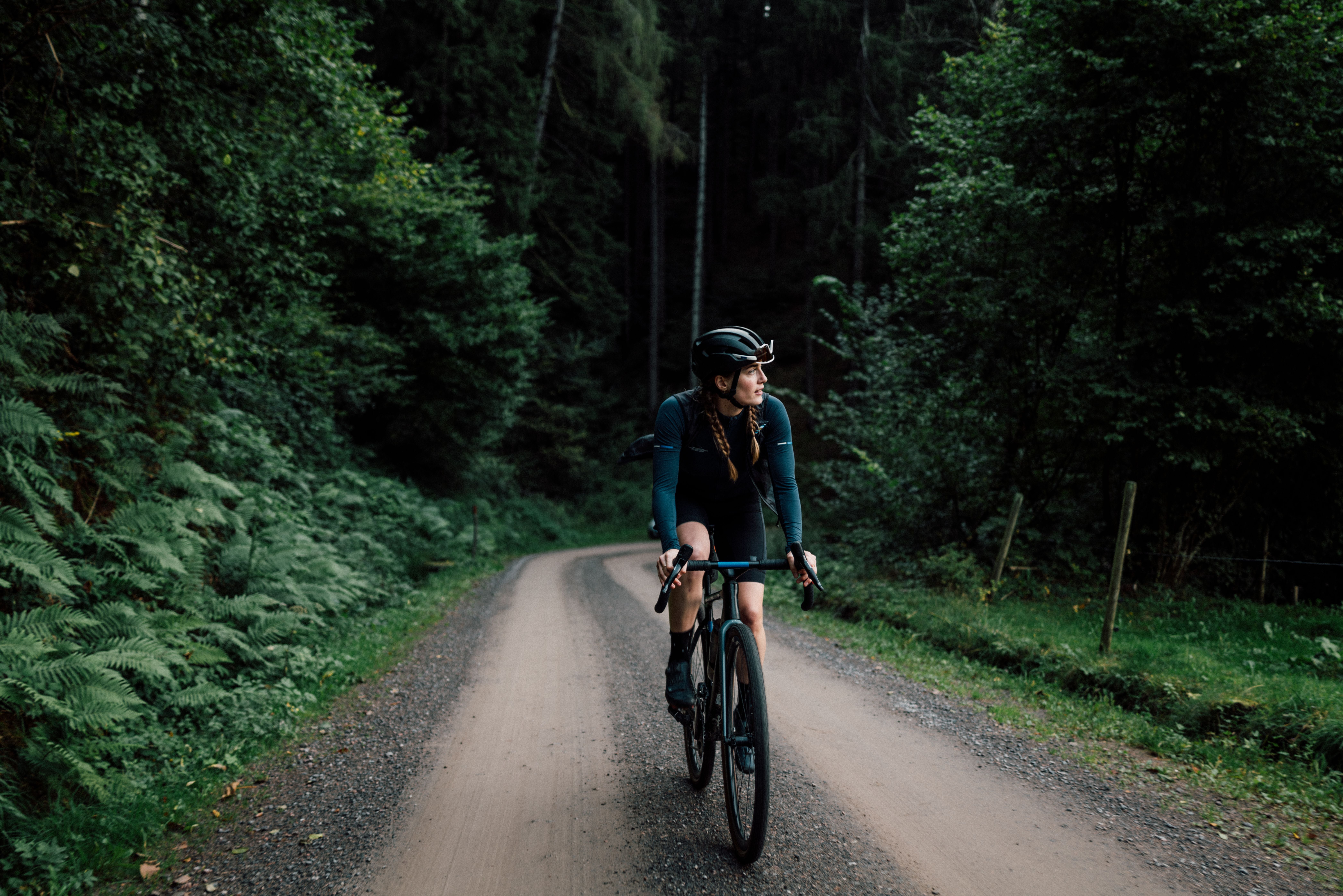 Radfahrerin in Sportkleidung fährt auf einem Schotterweg durch einen dichten, grünen Wald.