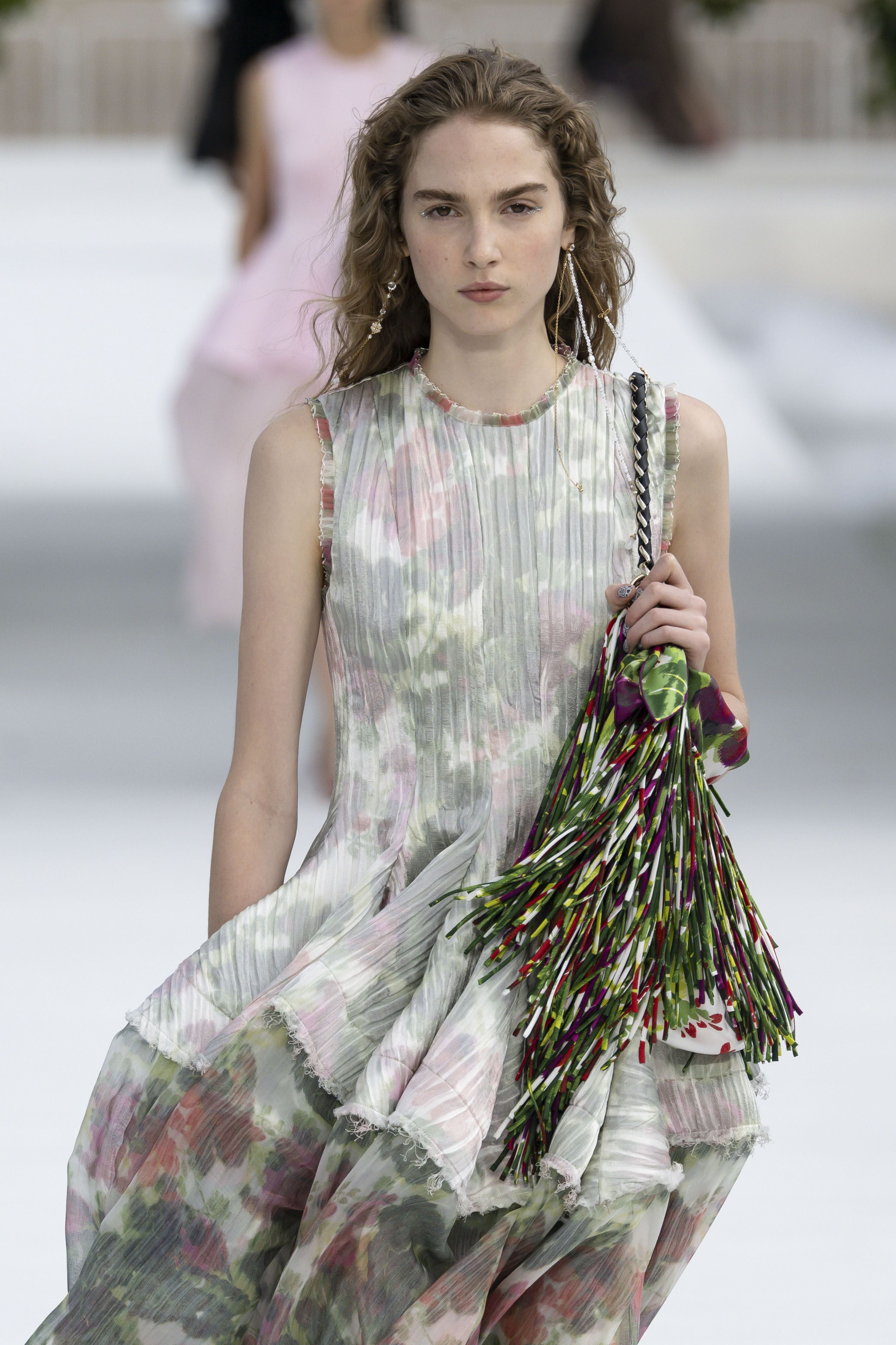 Model in fließendem, blumigem Kleid mit großer, bunter Quastentasche auf dem Laufsteg.