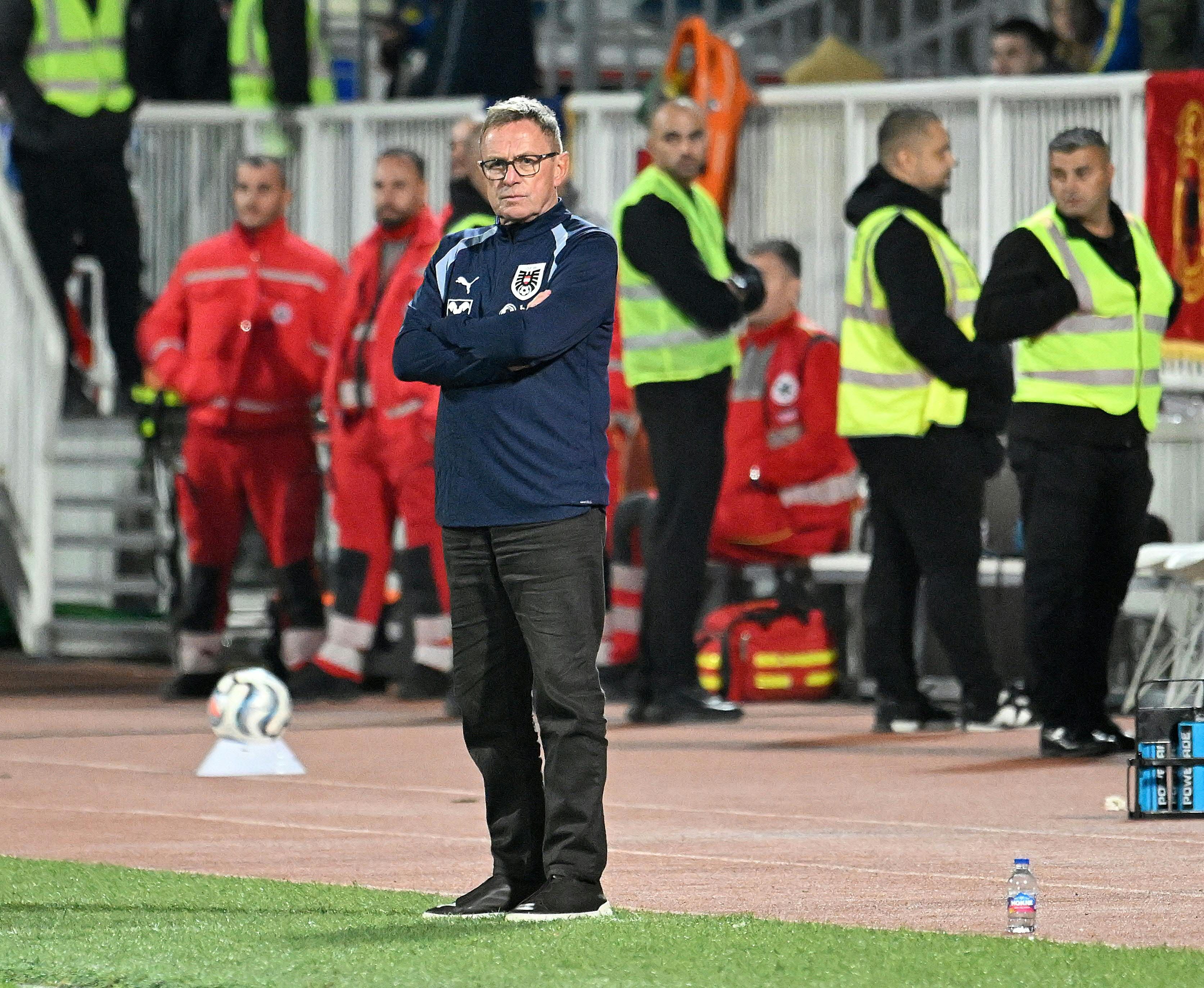 Trainer steht mit verschränkten Armen am Spielfeldrand, im Hintergrund Sanitäter und Ordner.