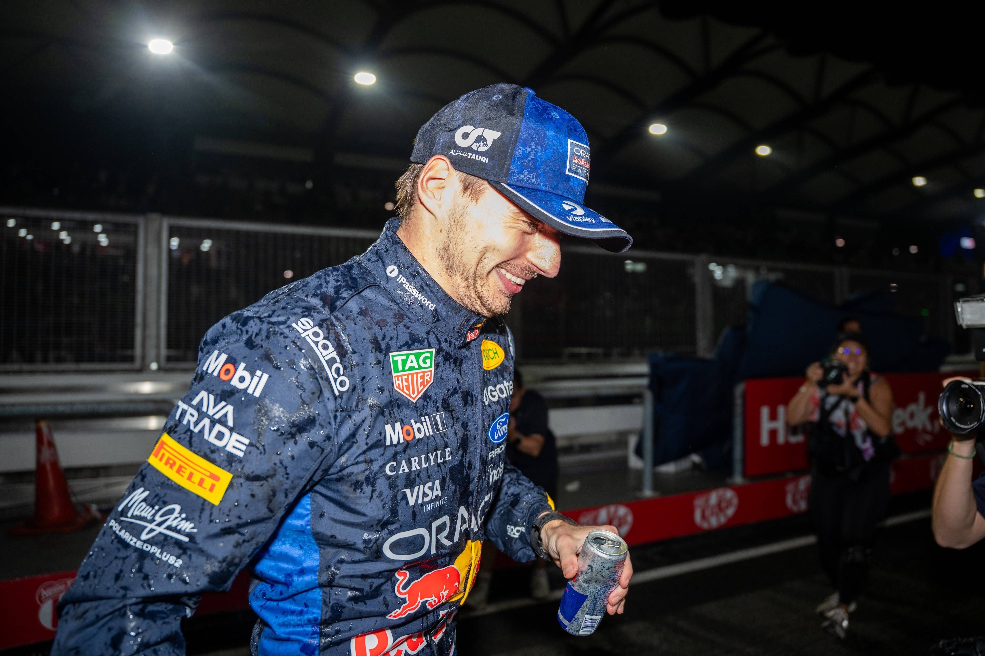 Ein Rennfahrer im nassen Overall feiert mit einer Getränkedose nach einem Formel-1-Rennen.