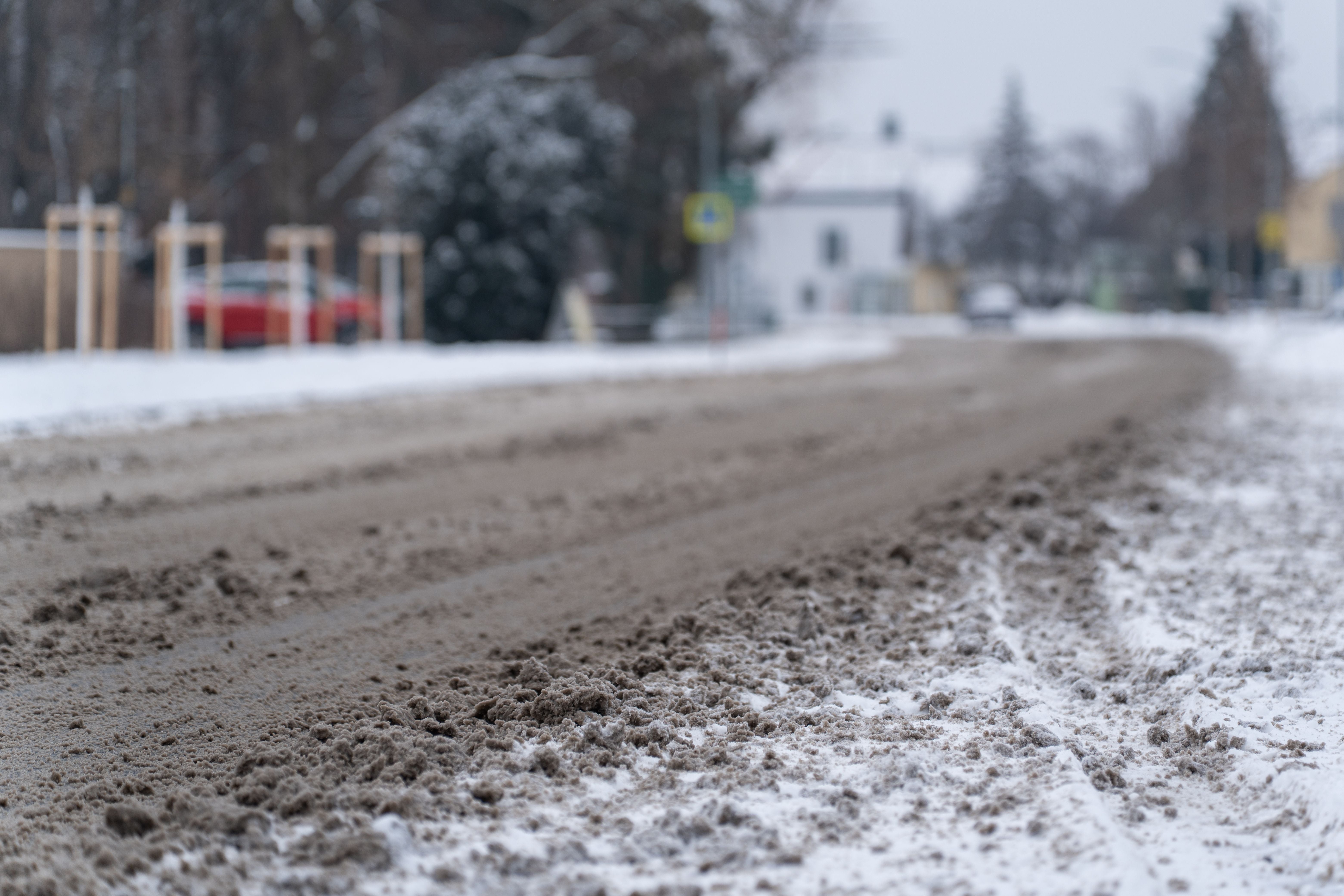 Verschneite Dorfstraße mit Matsch und Schneeresten an einem kalten Wintertag aus niedriger Perspektive.