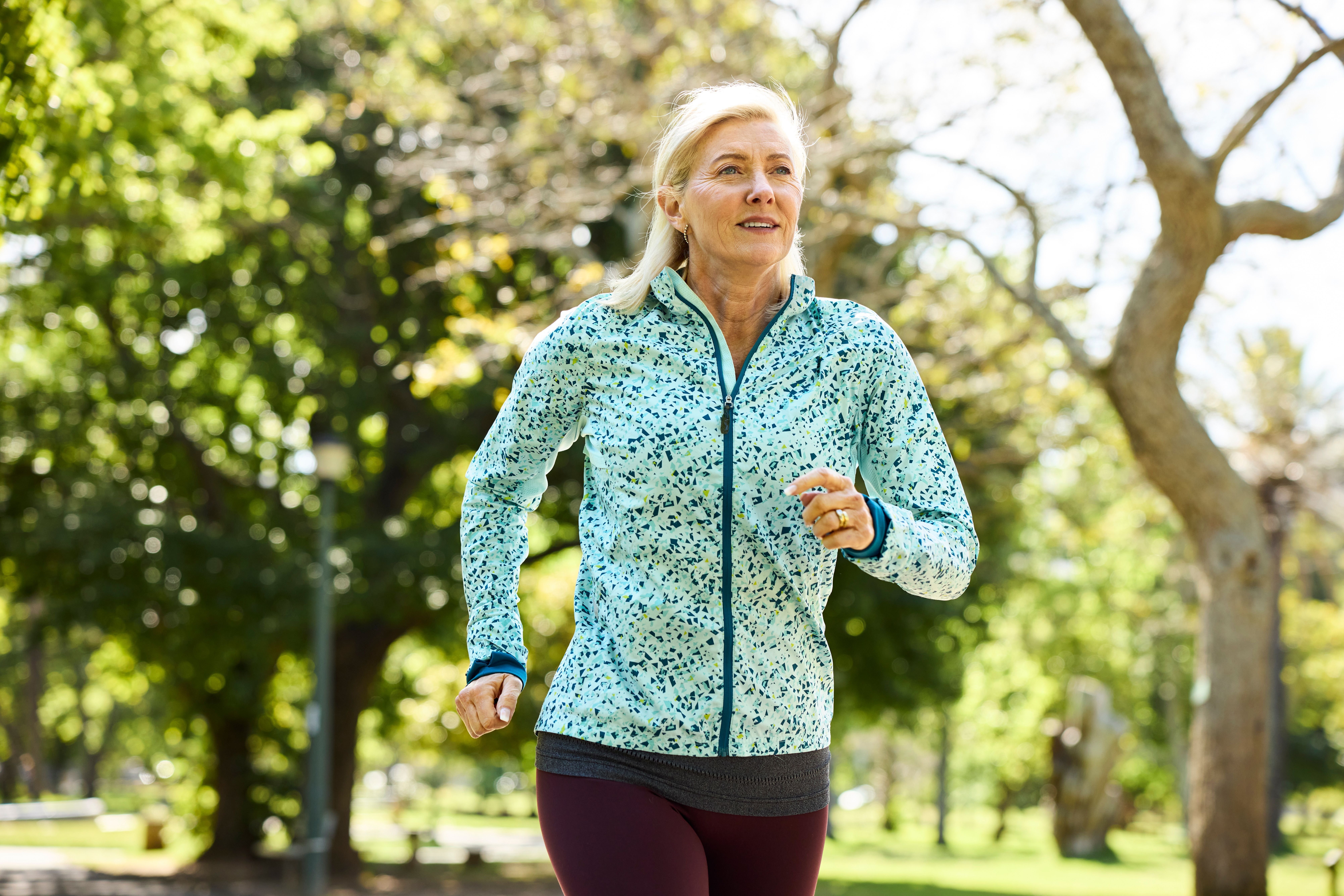 Ältere blonde Frau joggt morgens im Park und trägt sportliche Kleidung.