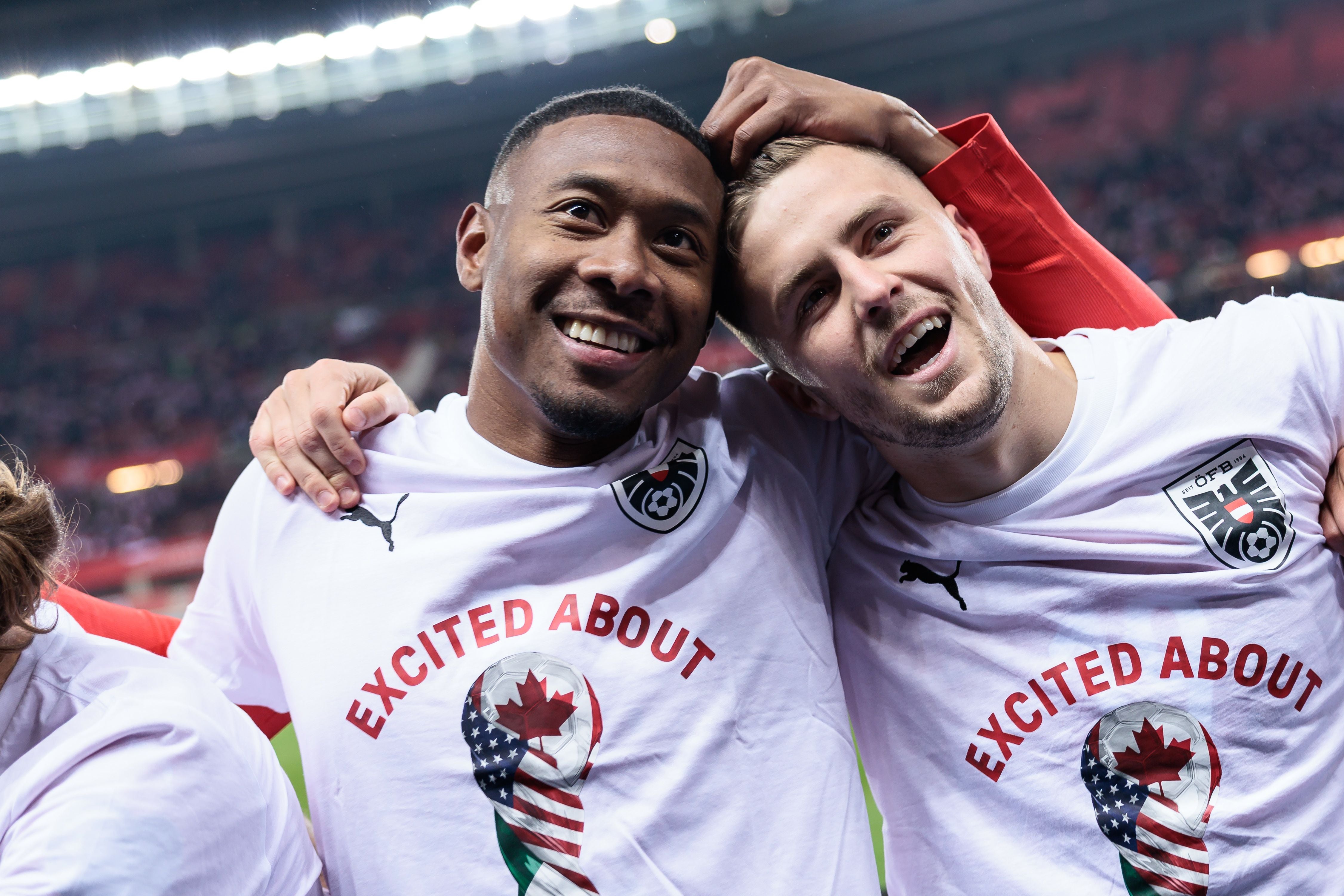 Zwei jubelnde Fußballspieler im weißen Trikot umarmen sich im Stadion.