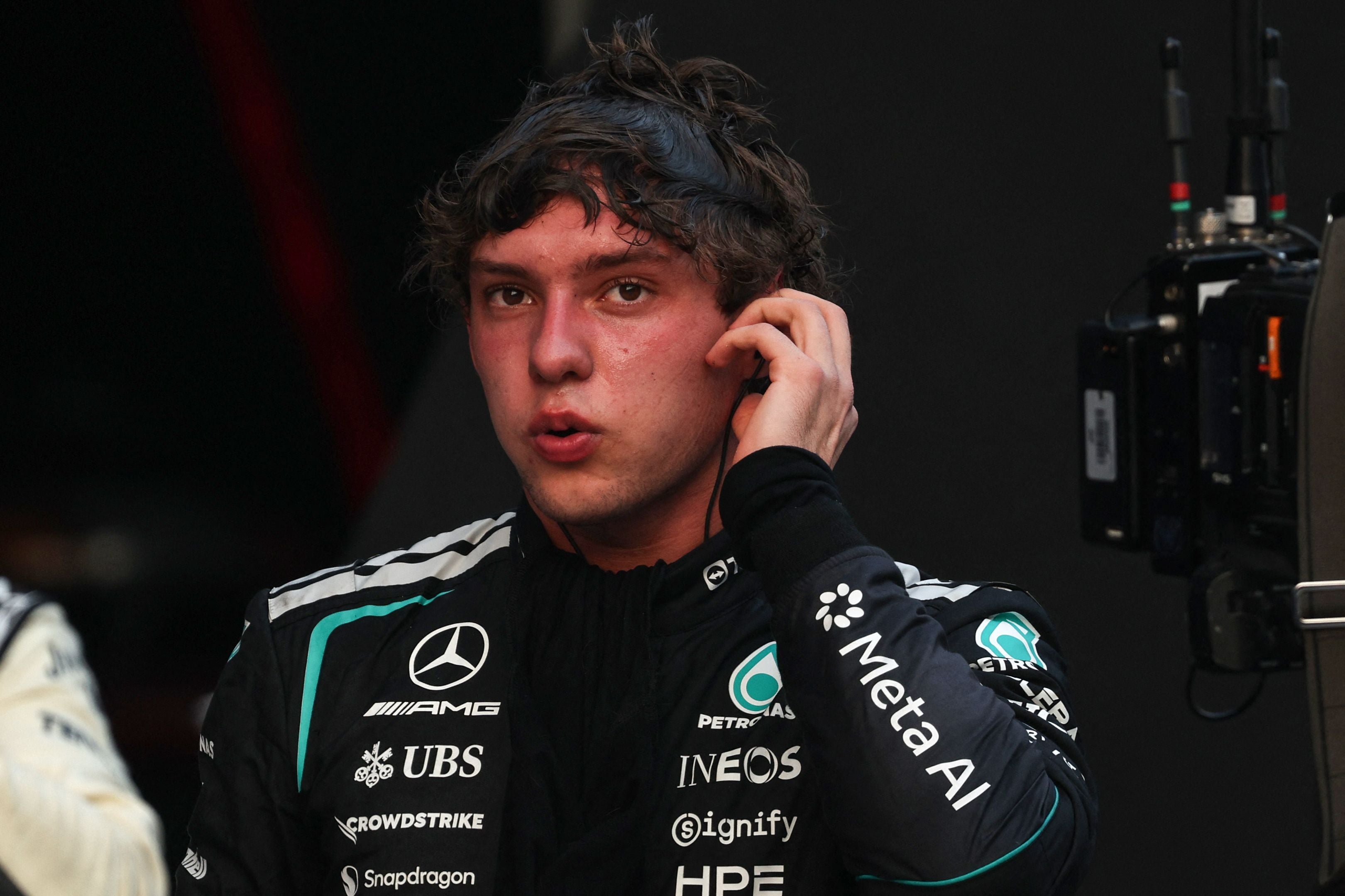 Ein Formel-1-Fahrer im Mercedes-Anzug berührt sein Ohr und blickt konzentriert zur Seite.