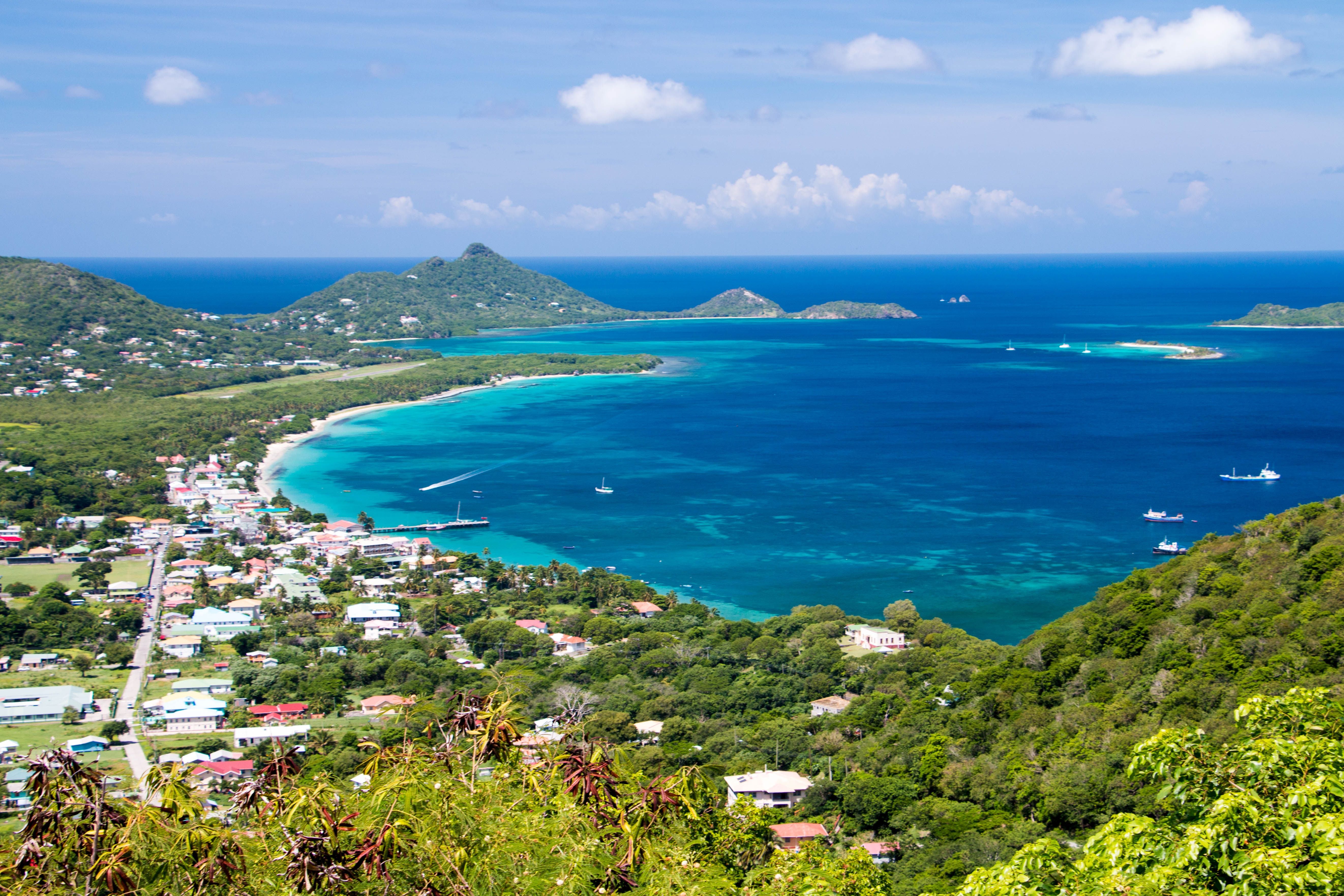 Blick auf eine Küstenstadt in Grenada mit türkisblauem Meer und grünen Hügeln.