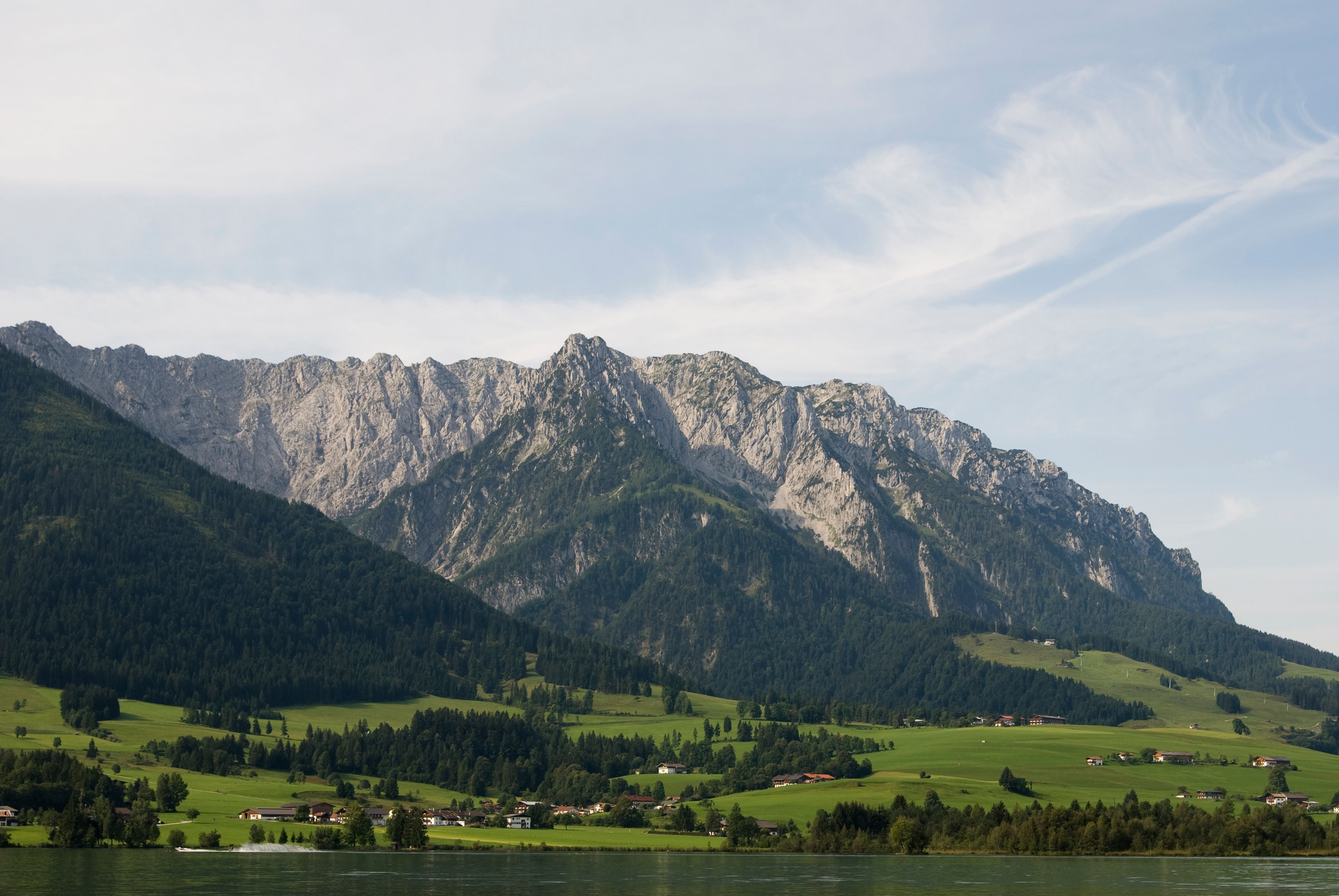 Blick auf den Zahmen Kaiser mit grünen Wiesen, Wald und verstreuten Häusern im Vordergrund.