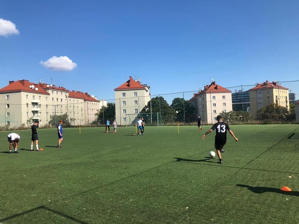 Mehrere Jugendliche trainieren Fußball auf einem Kunstrasenplatz bei sonnigem Wetter.