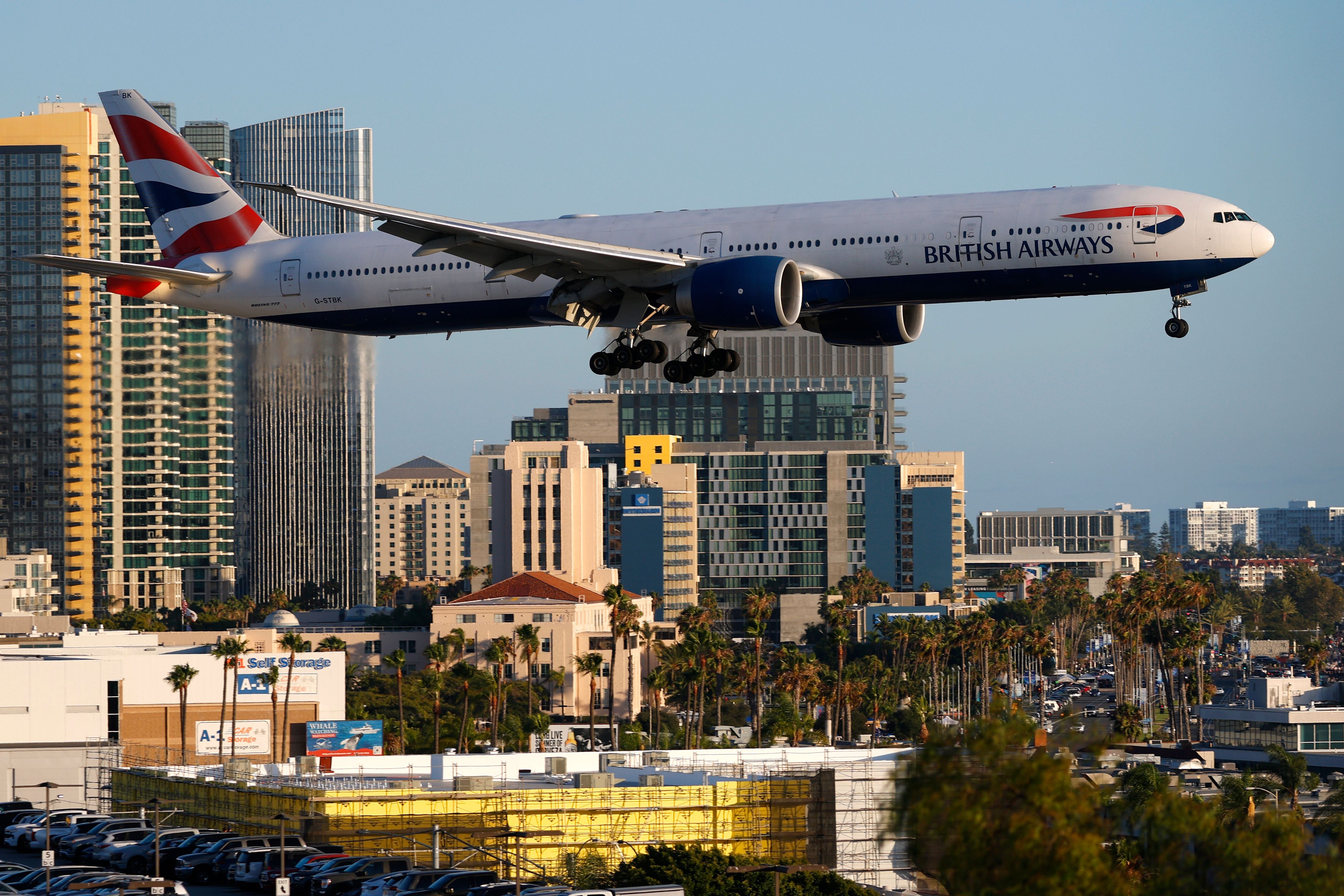 Ein British Airways Boeing 777 landet nahe Hochhäusern am Flughafen San Diego bei Tageslicht.