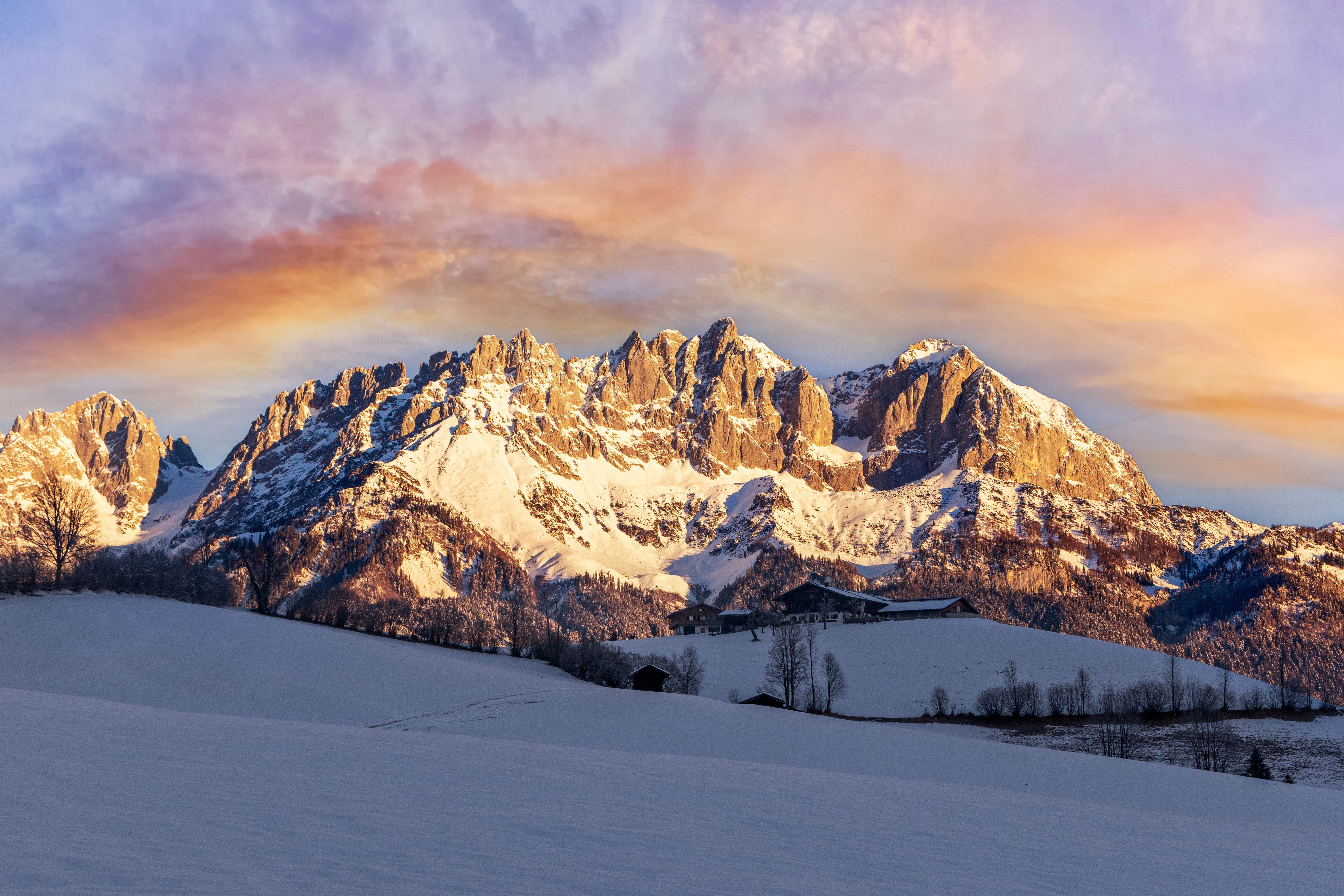 Verschneite Berge bei Sonnenuntergang in Ellmau, Tirol, mit Hütten im Vordergrund.