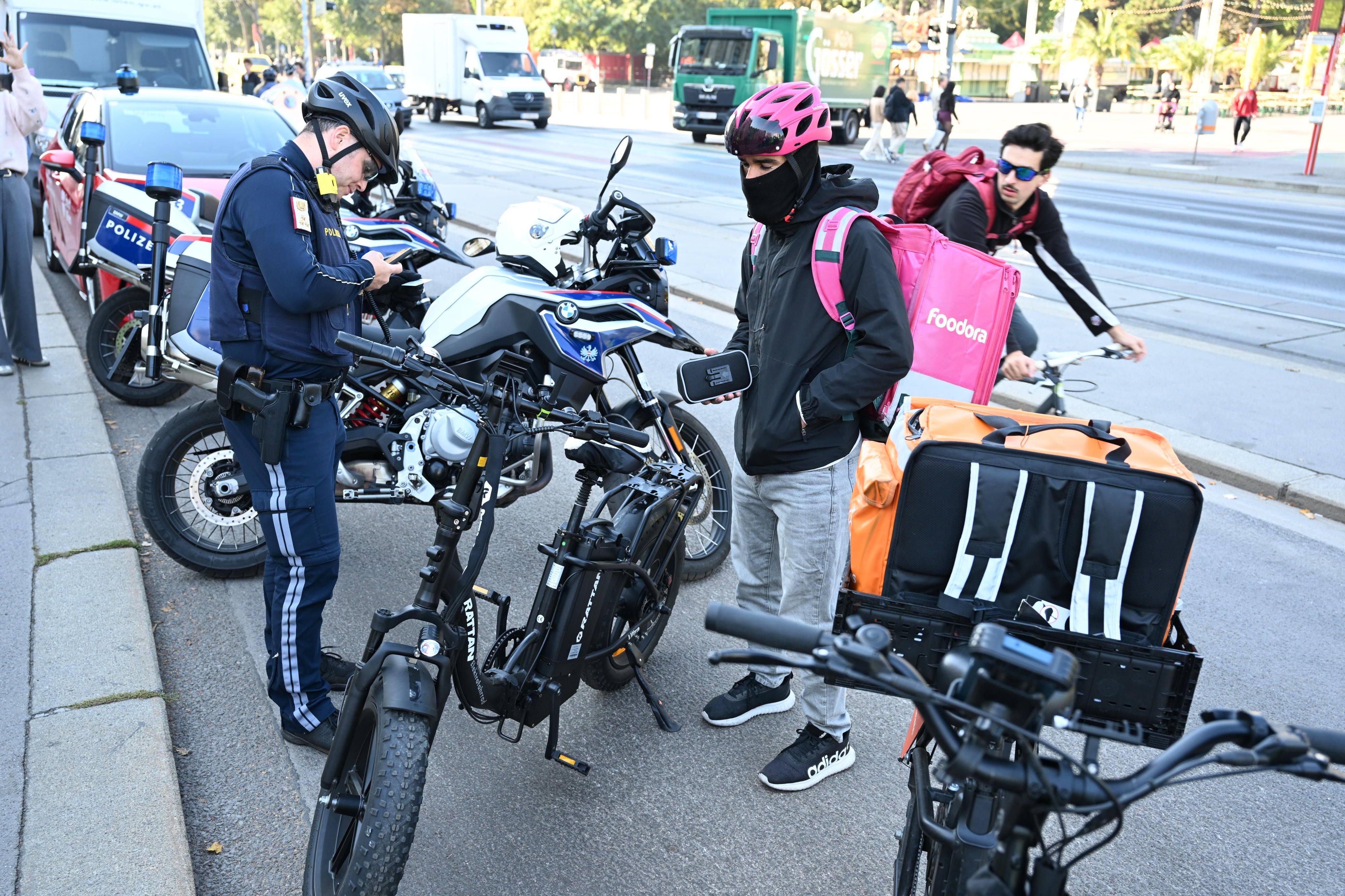 Polizist kontrolliert E-Moped-Fahrer mit Lieferrucksack auf einer Straße in der Stadt.