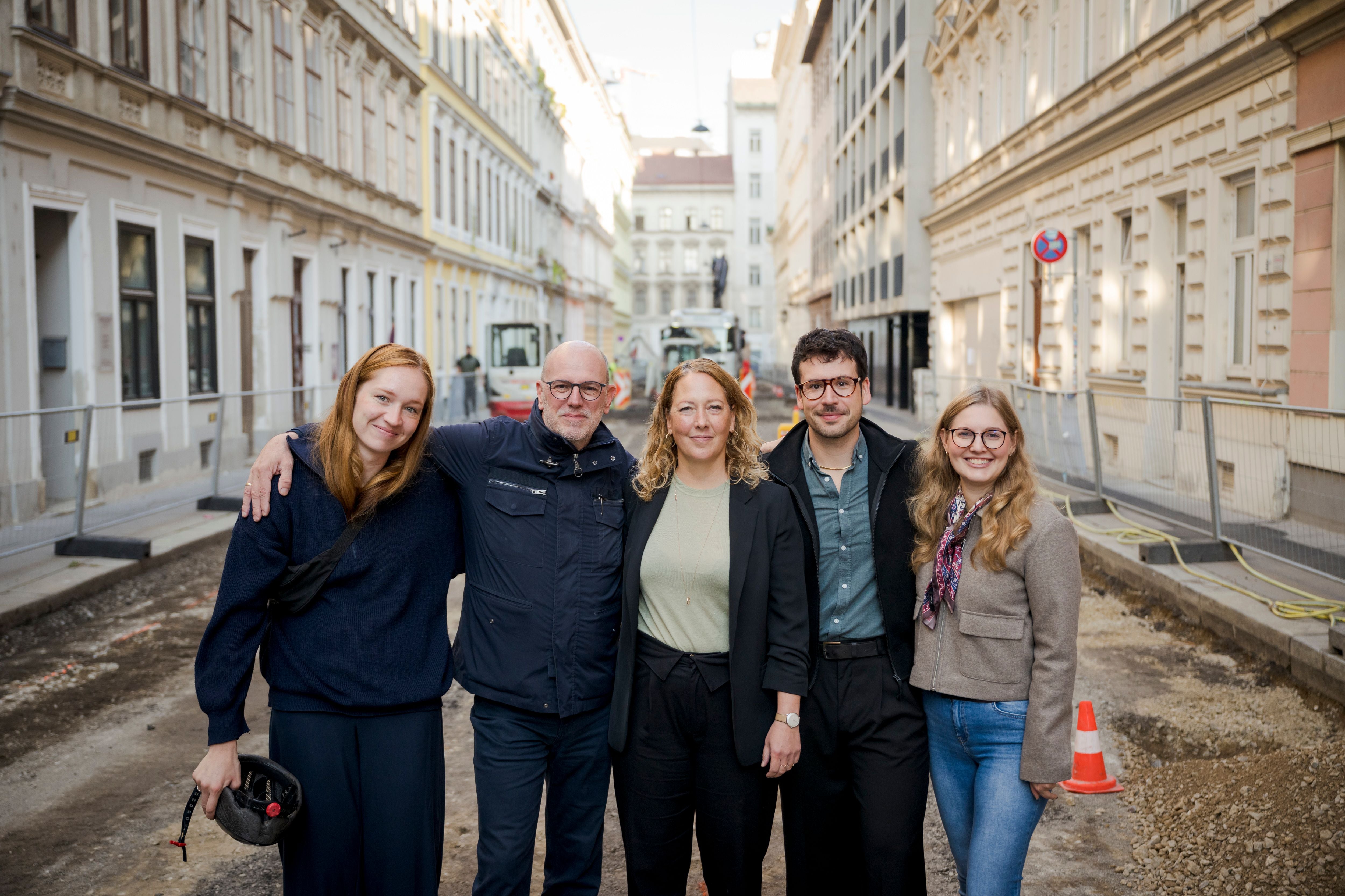 Fünf Personen posieren lächelnd auf einer Baustelle in einer Straße der Rüdigergasse.