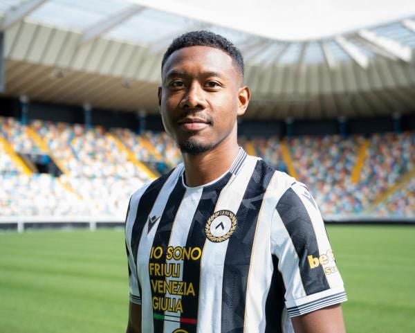 Ein Fußballspieler im schwarz-weißen Trikot von Udinese steht im Stadion.