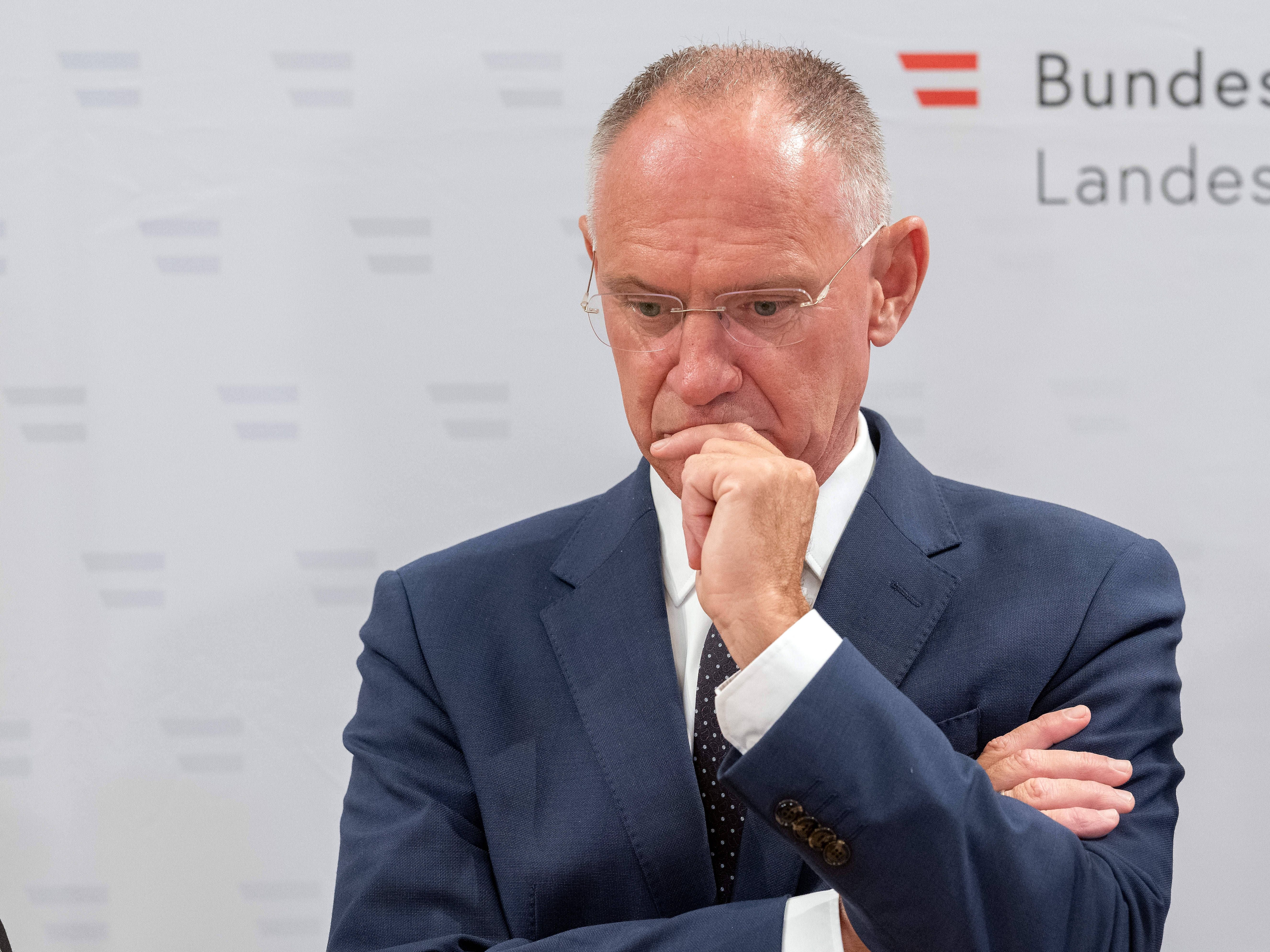Mann im Anzug steht nachdenklich mit verschränkten Armen bei einer Präsentation in Wien.