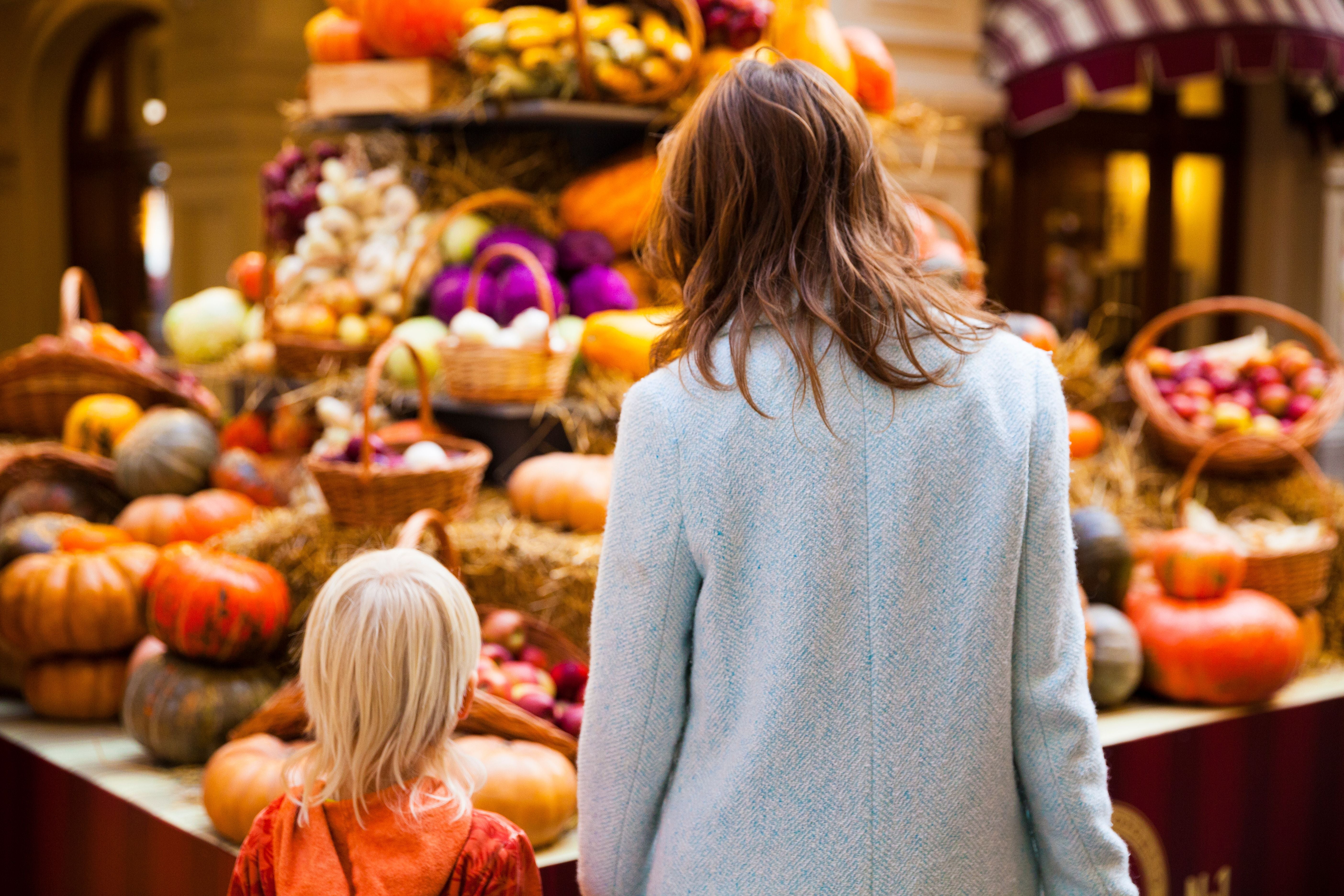 Frau und Kind betrachten einen bunten Erntetisch mit Kürbissen und Gemüse auf dem Markt.