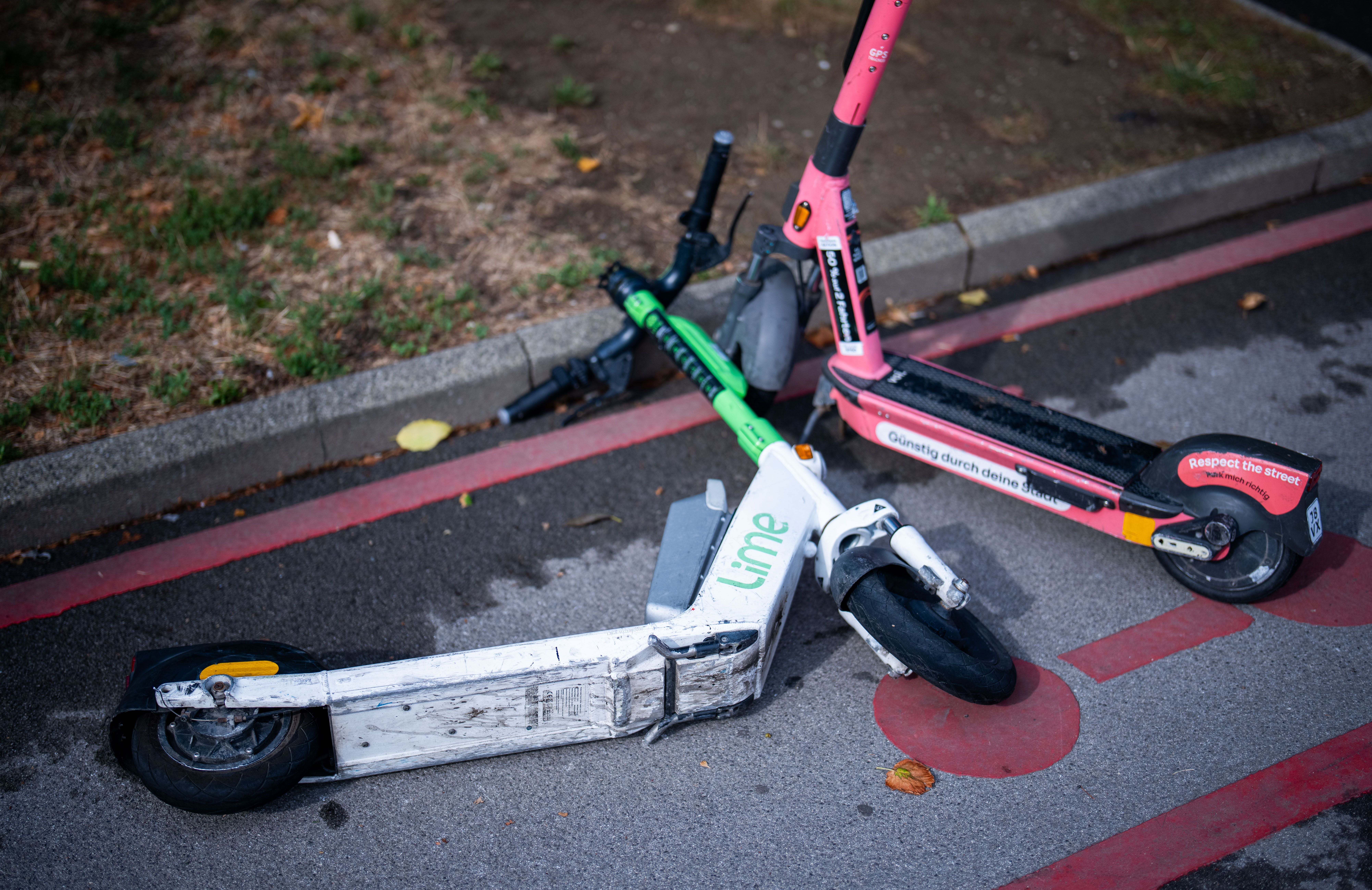 Drei E-Scooter liegen umgekippt auf einem markierten Abstellplatz am Straßenrand.