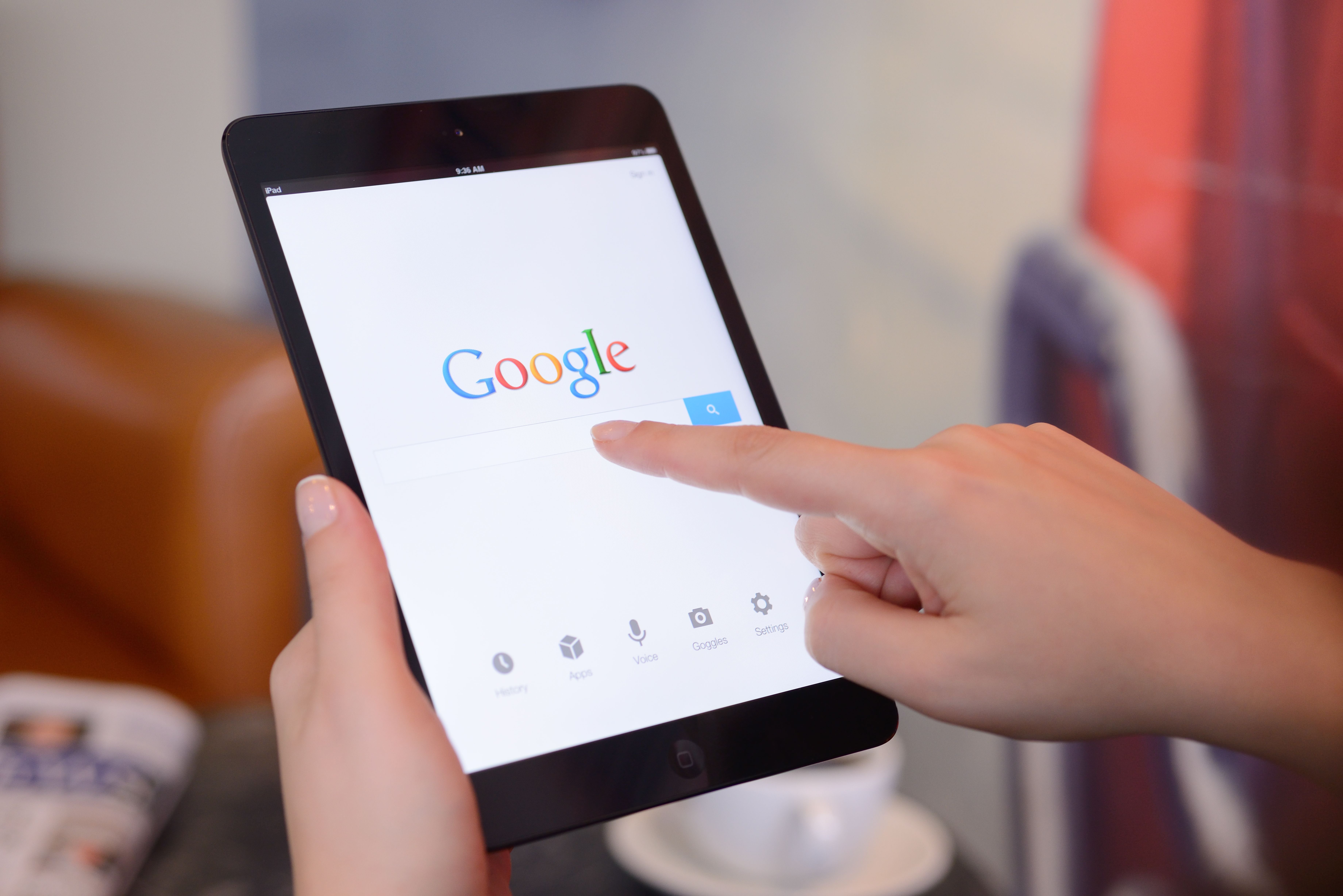 Eine Person benutzt ein iPad Mini mit geöffneter Google-Suchseite in einem Café.