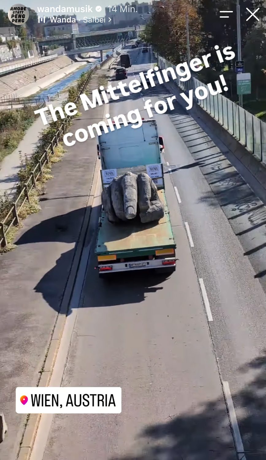 Ein LKW transportiert eine große Mittelfinger-Skulptur durch eine Straße in Wien.