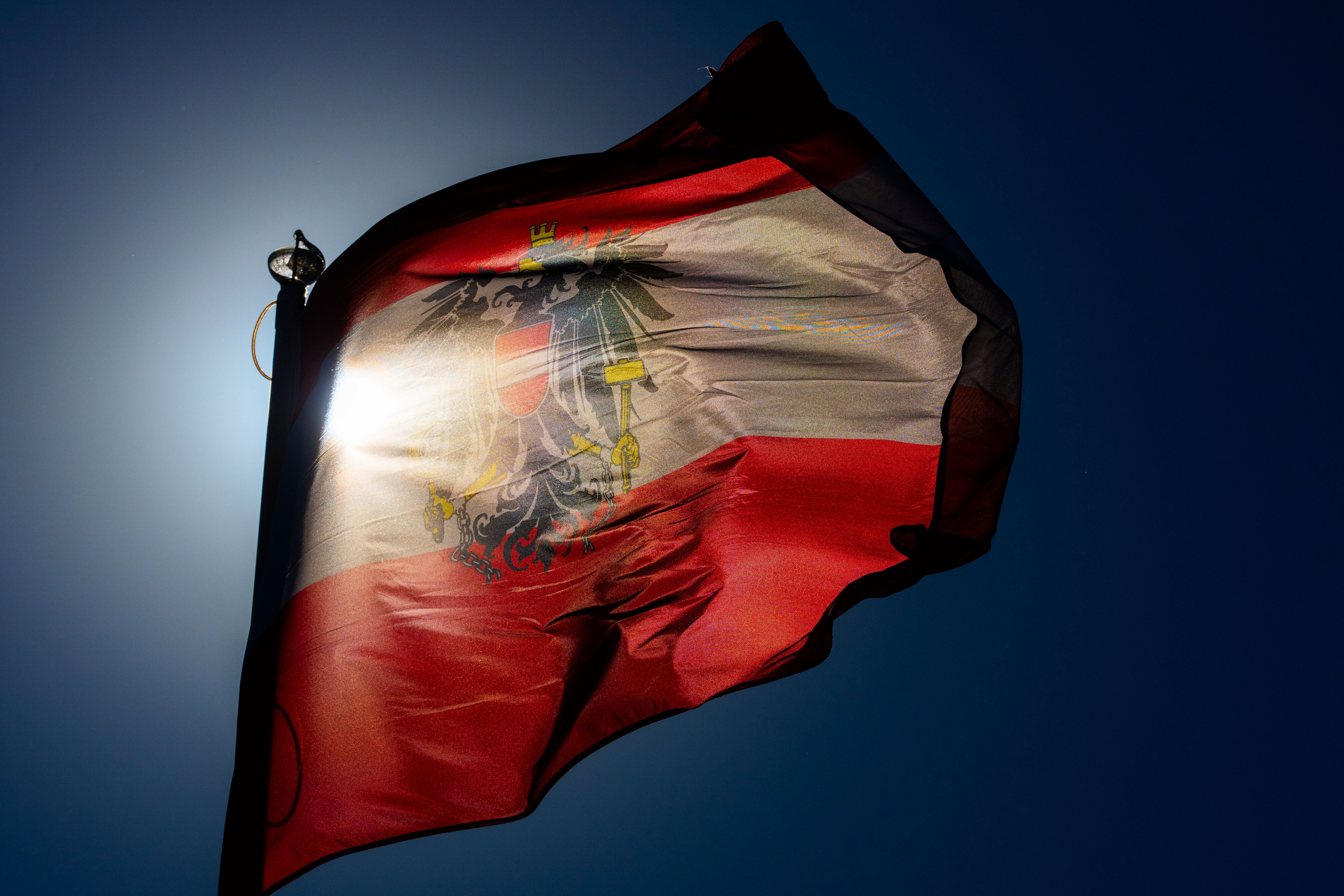 Die österreichische Flagge mit Wappen weht vor sonnigem, blauem Himmel.