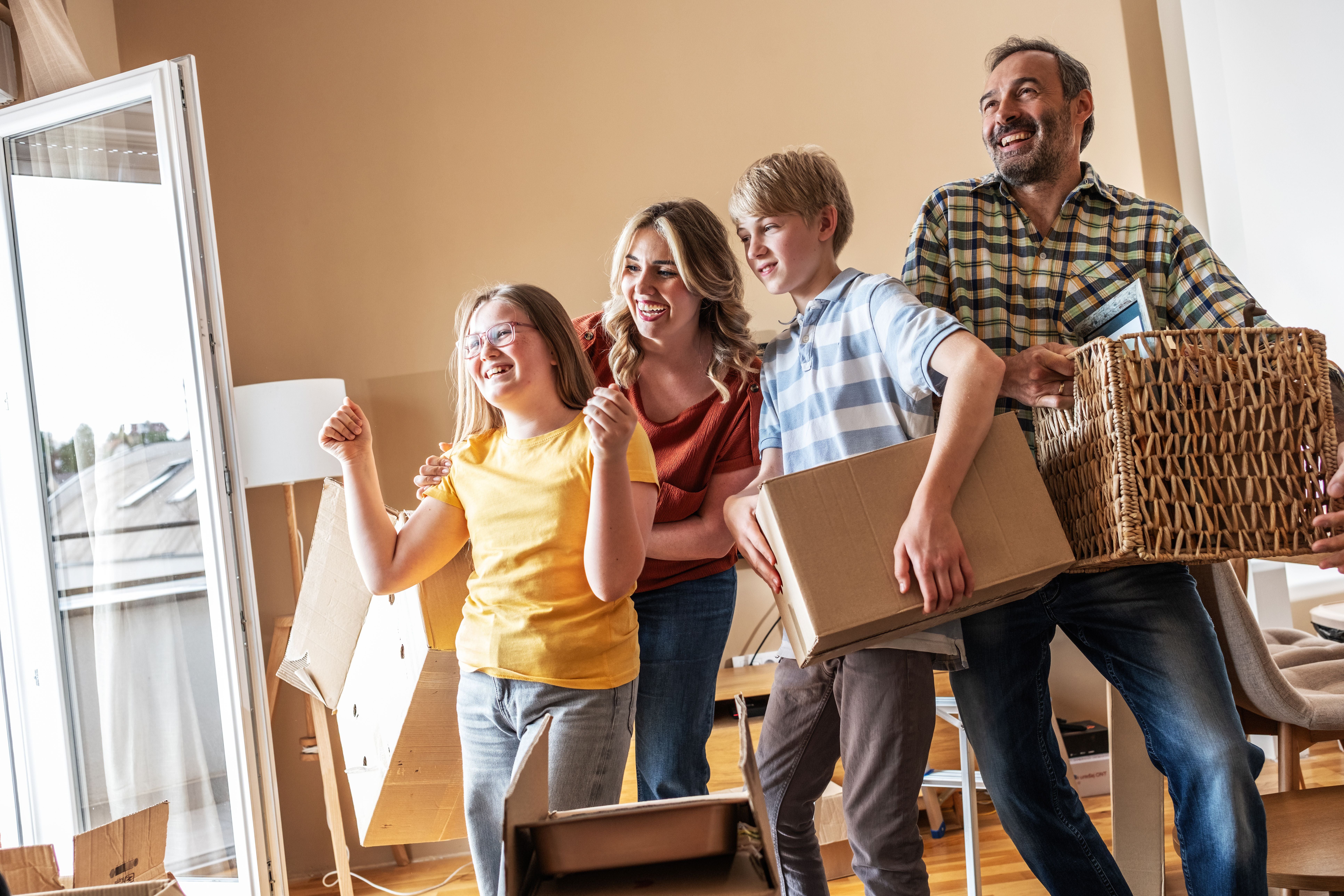 Eine Familie räumt gemeinsam Umzugskartons im neuen Wohnzimmer aus und lacht glücklich.