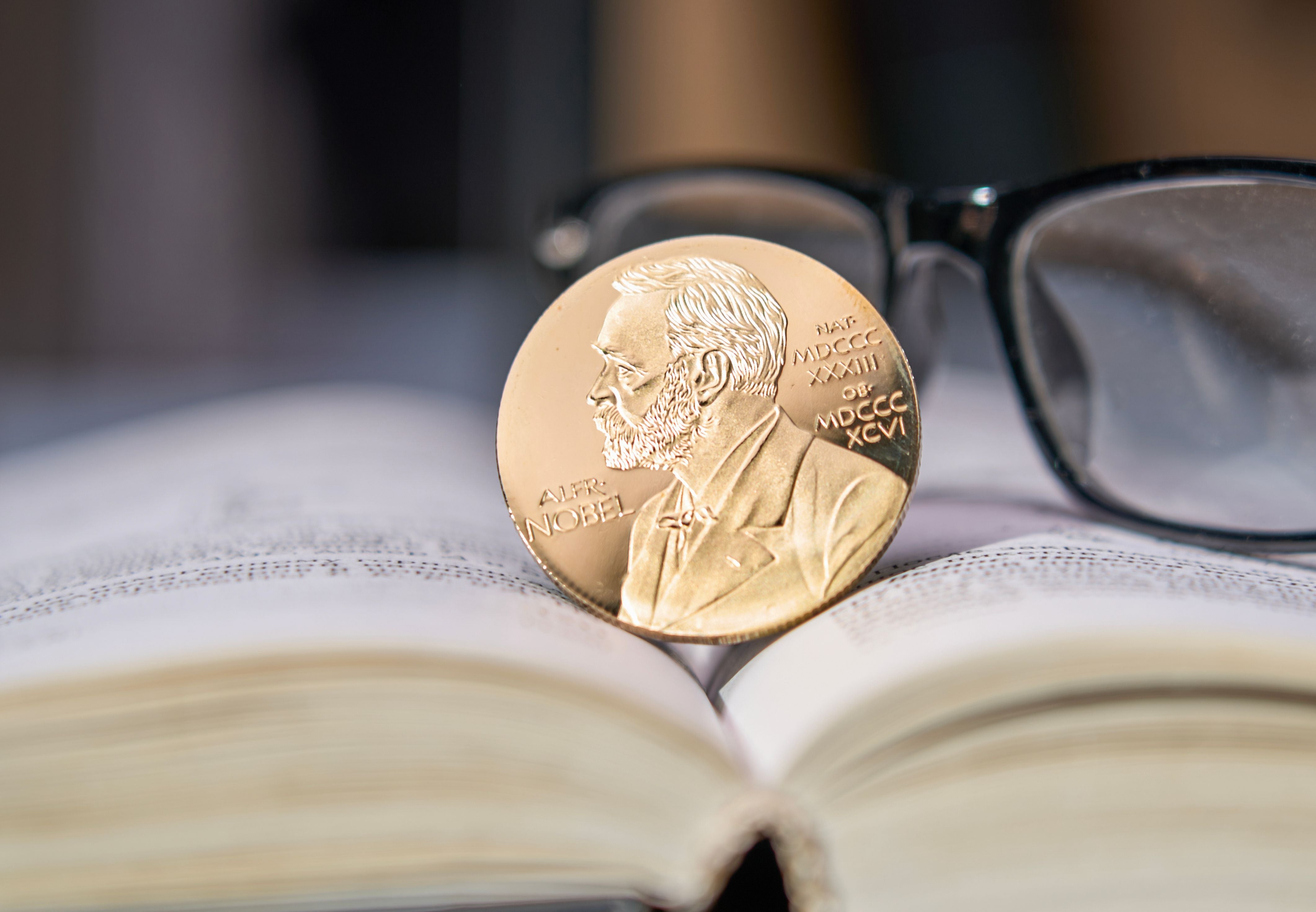Nobelpreis-Medaille auf einem offenen Buch mit Brille im Hintergrund.