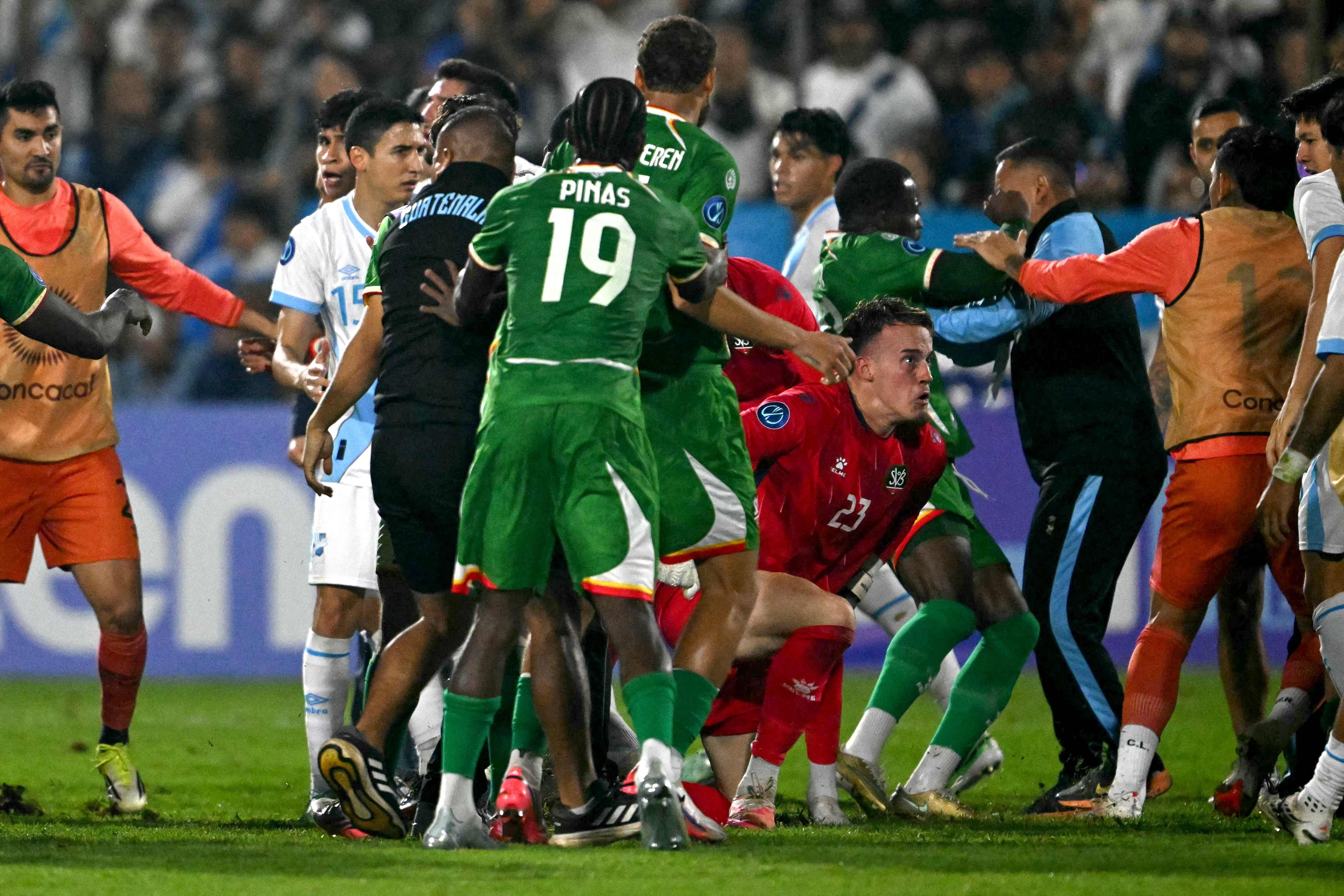 Spieler aus Guatemala und Suriname streiten am Spielfeldrand nach einem Fußballspiel.
