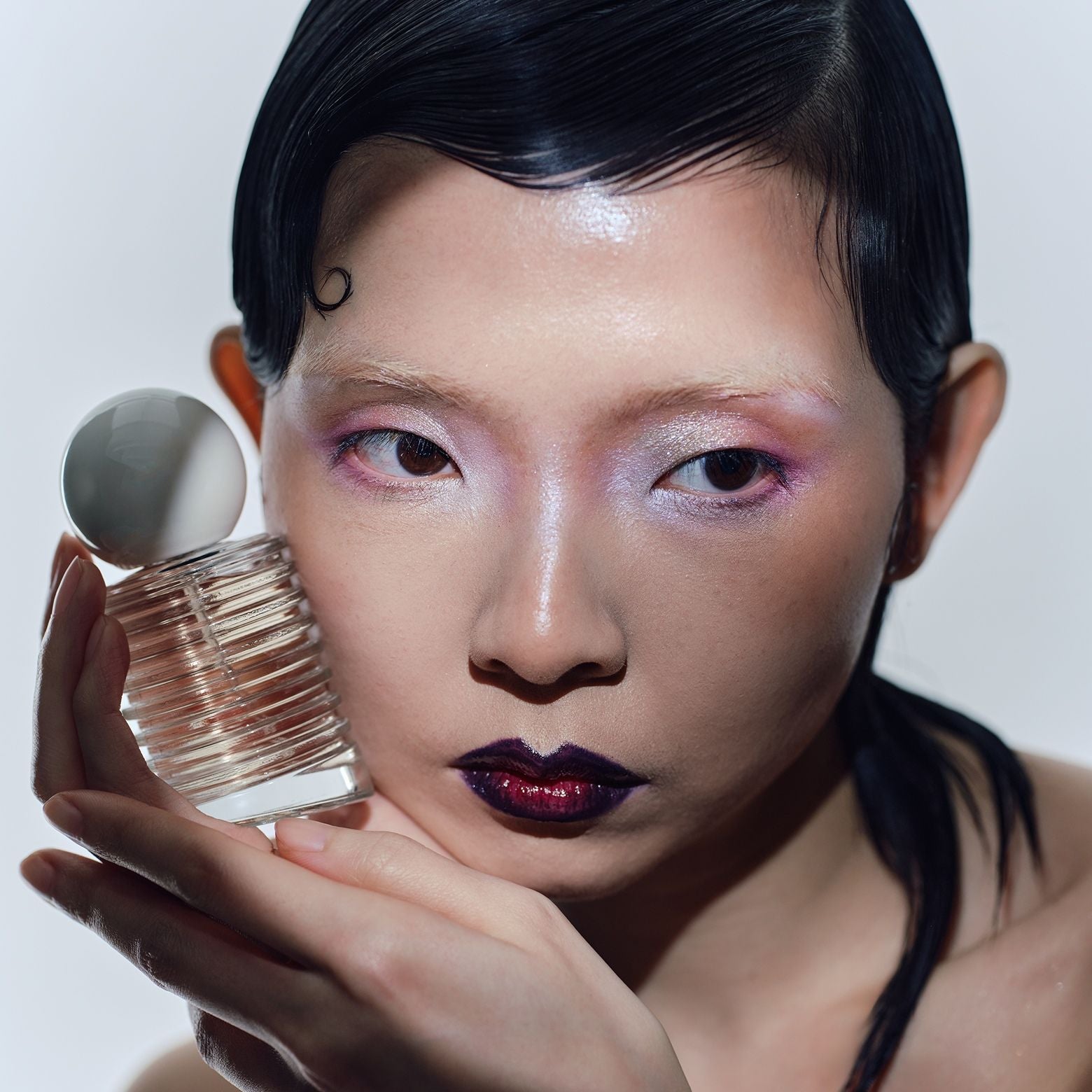 Person mit auffälligem Make-up hält ein Parfümflakon nah an das Gesicht.