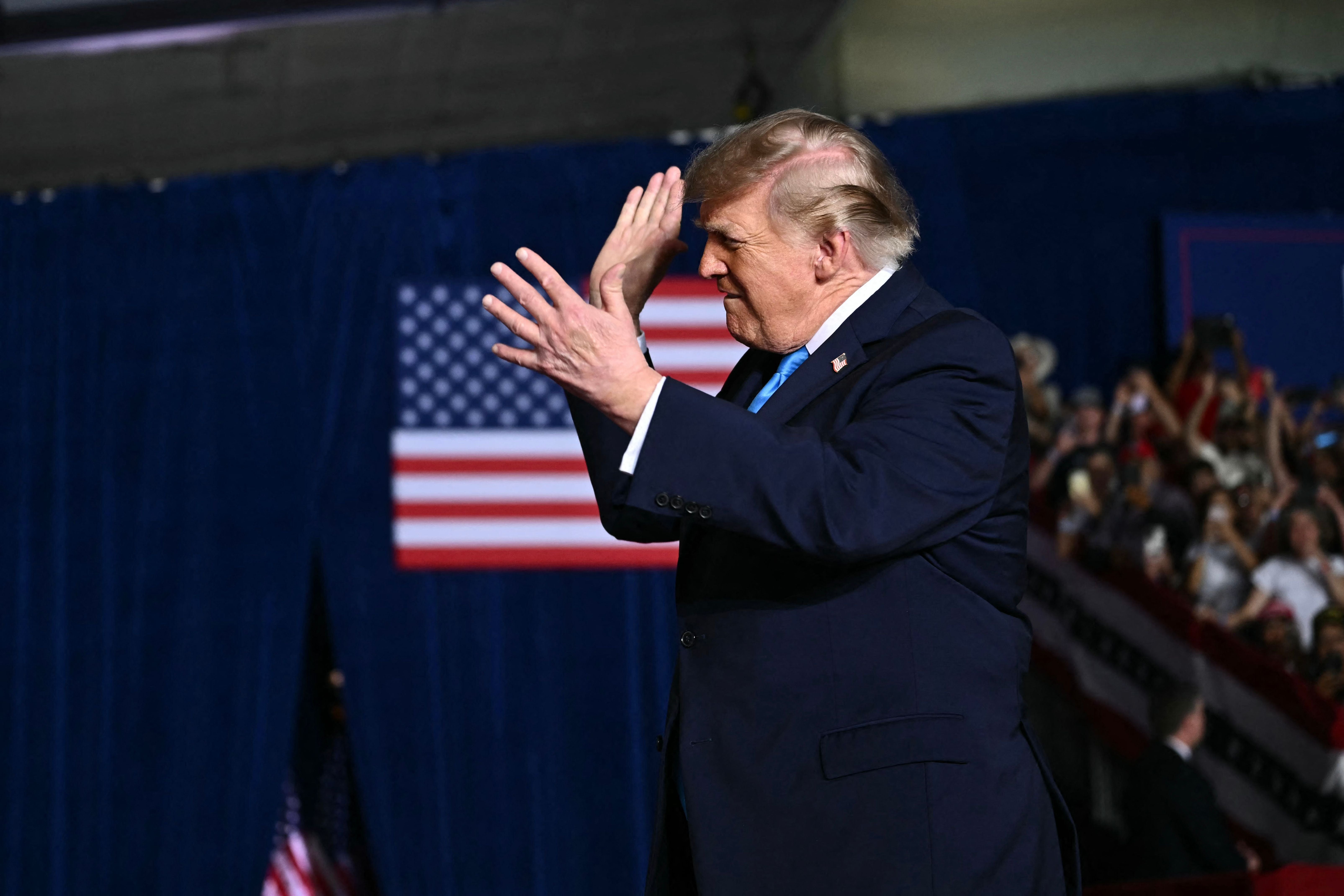 Ein Mann im Anzug klatscht auf einer Bühne vor einer amerikanischen Flagge.