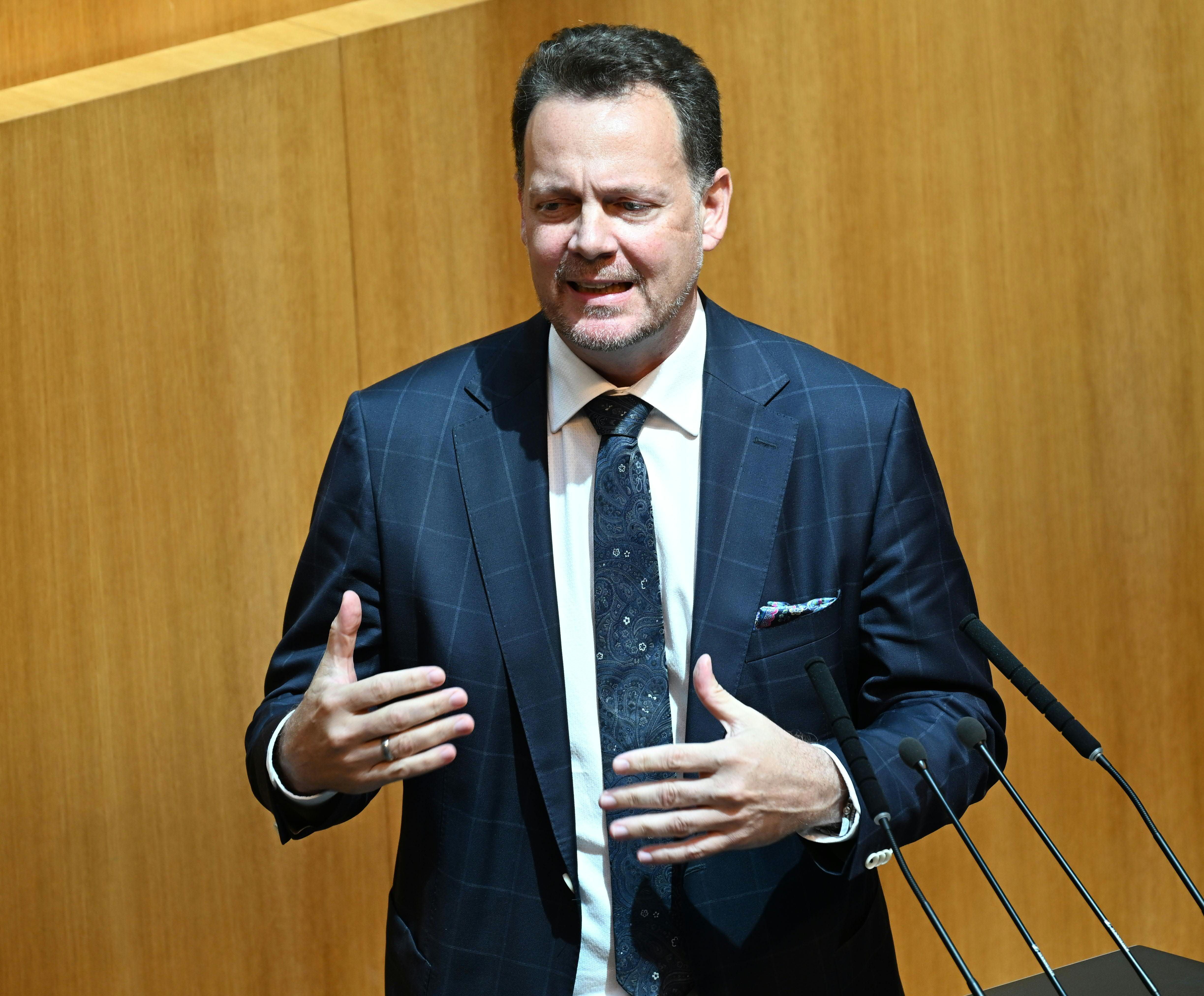 Ein Mann im Anzug spricht gestikulierend an einem Rednerpult im Parlament.