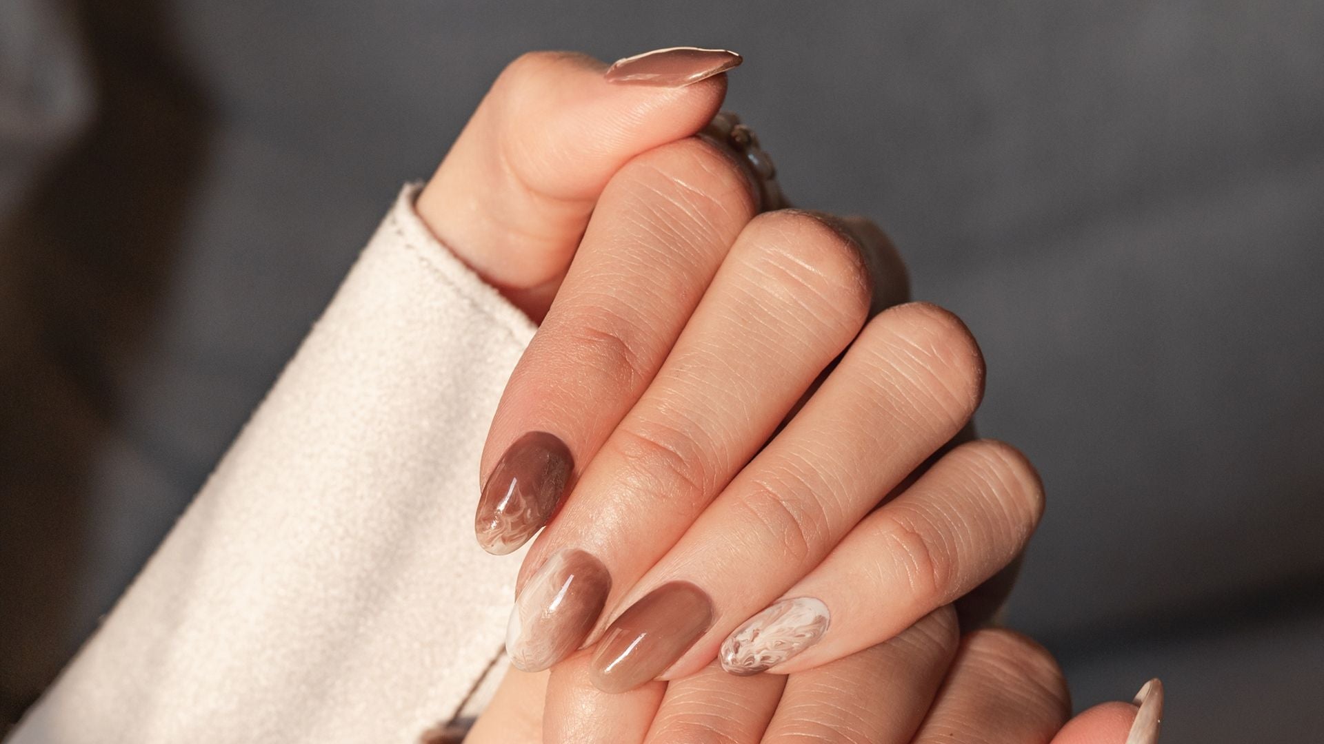 Hände mit langen, braun und beige gemusterten Fingernägeln im Nahaufnahme.