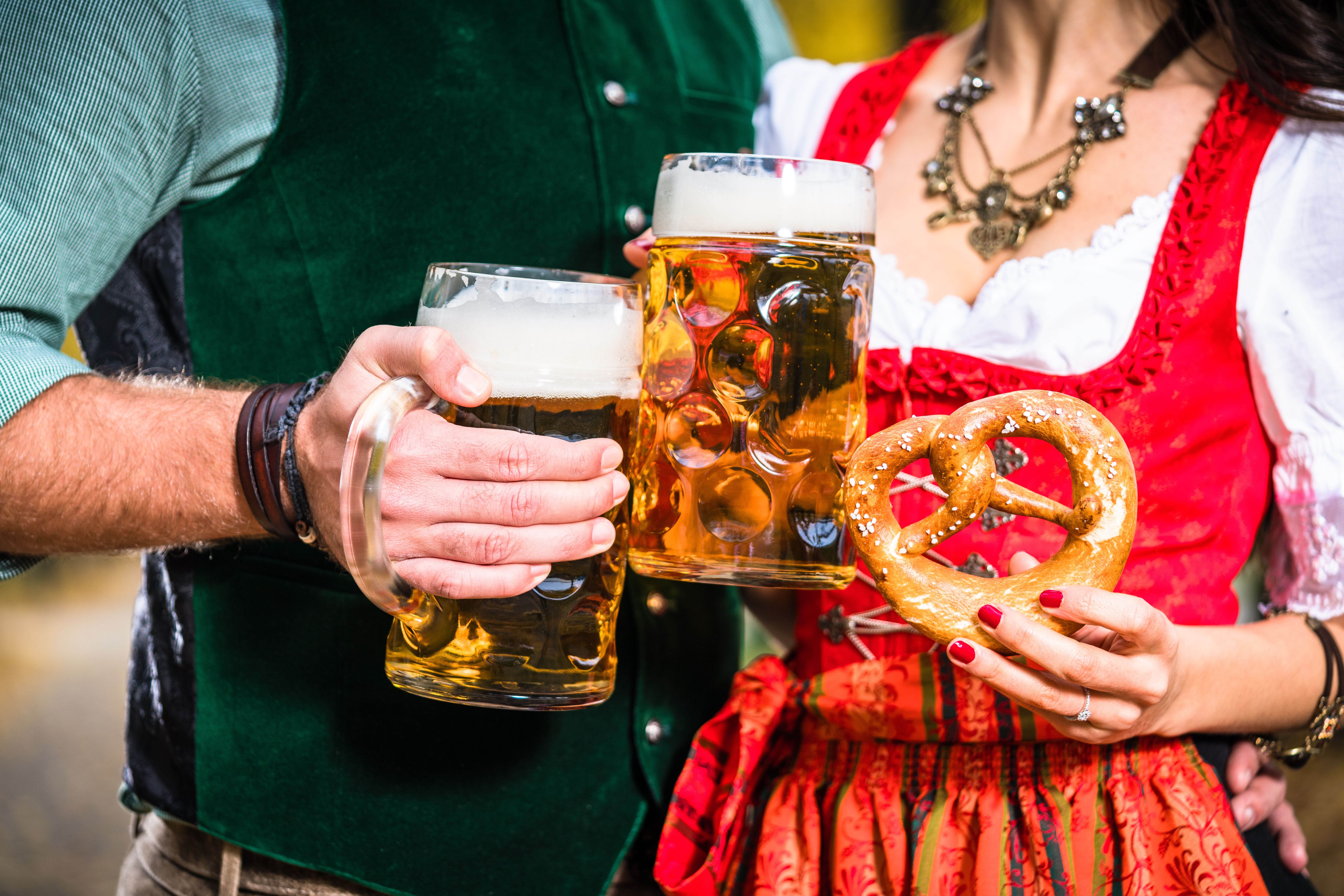 Zwei Personen in Tracht halten Maß Bier und eine Brezel, Oktoberfest-Atmosphäre.