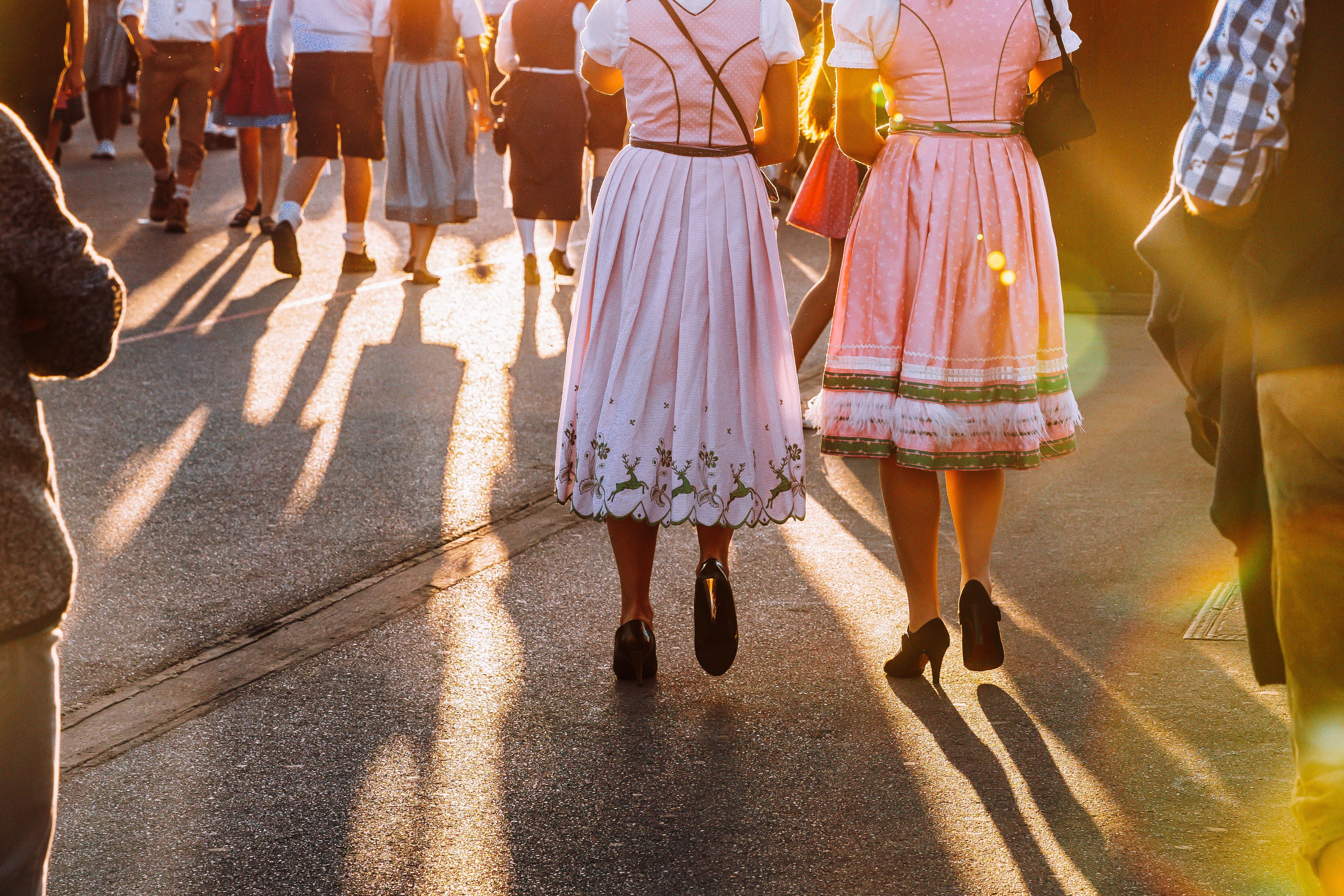 Zwei Frauen in Dirndlkleidern gehen bei Sonnenuntergang über das Oktoberfest-Gelände.