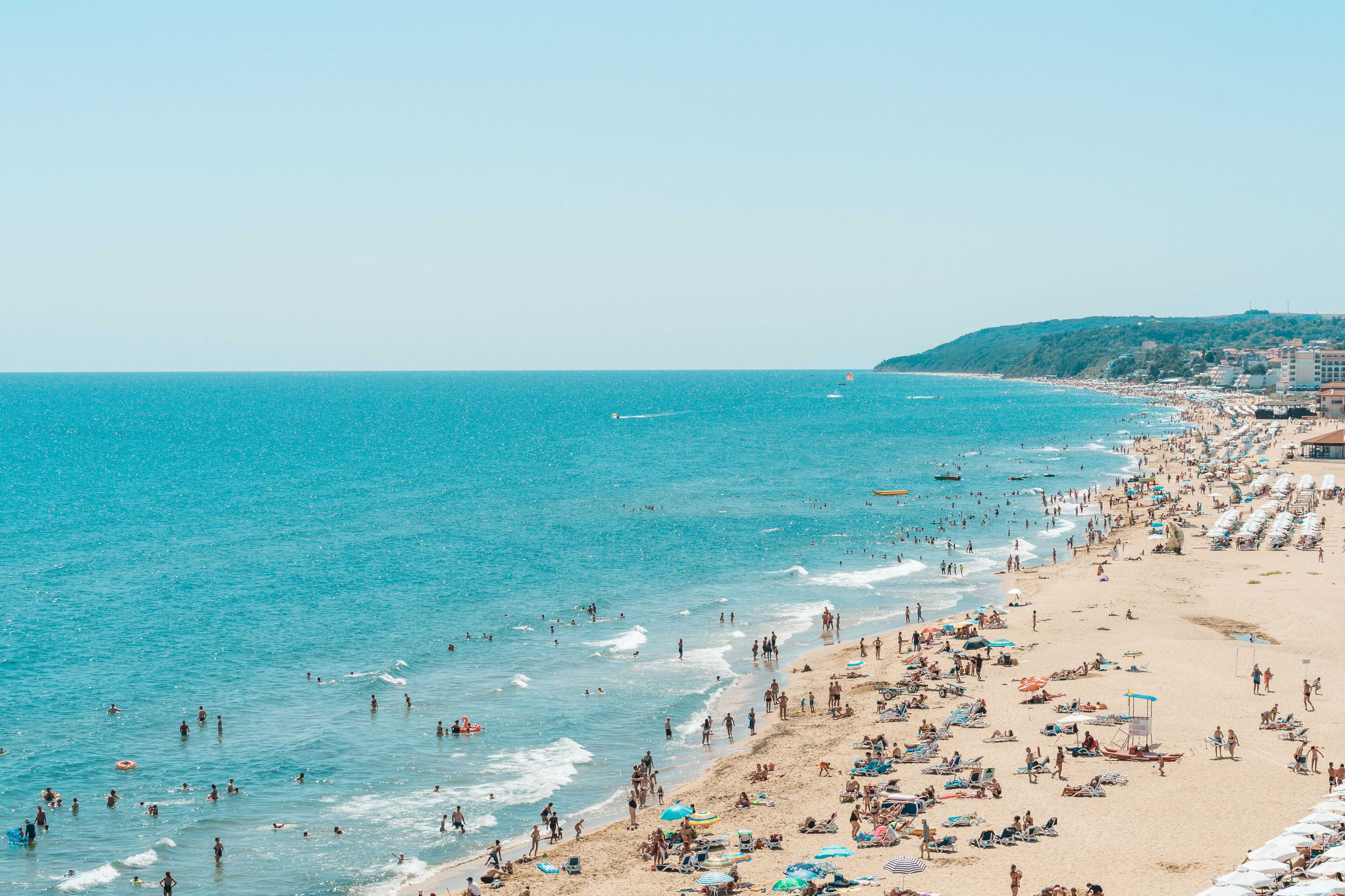 Voller Sandstrand mit Sonnenschirmen und vielen Menschen am Meer bei sonnigem Wetter.